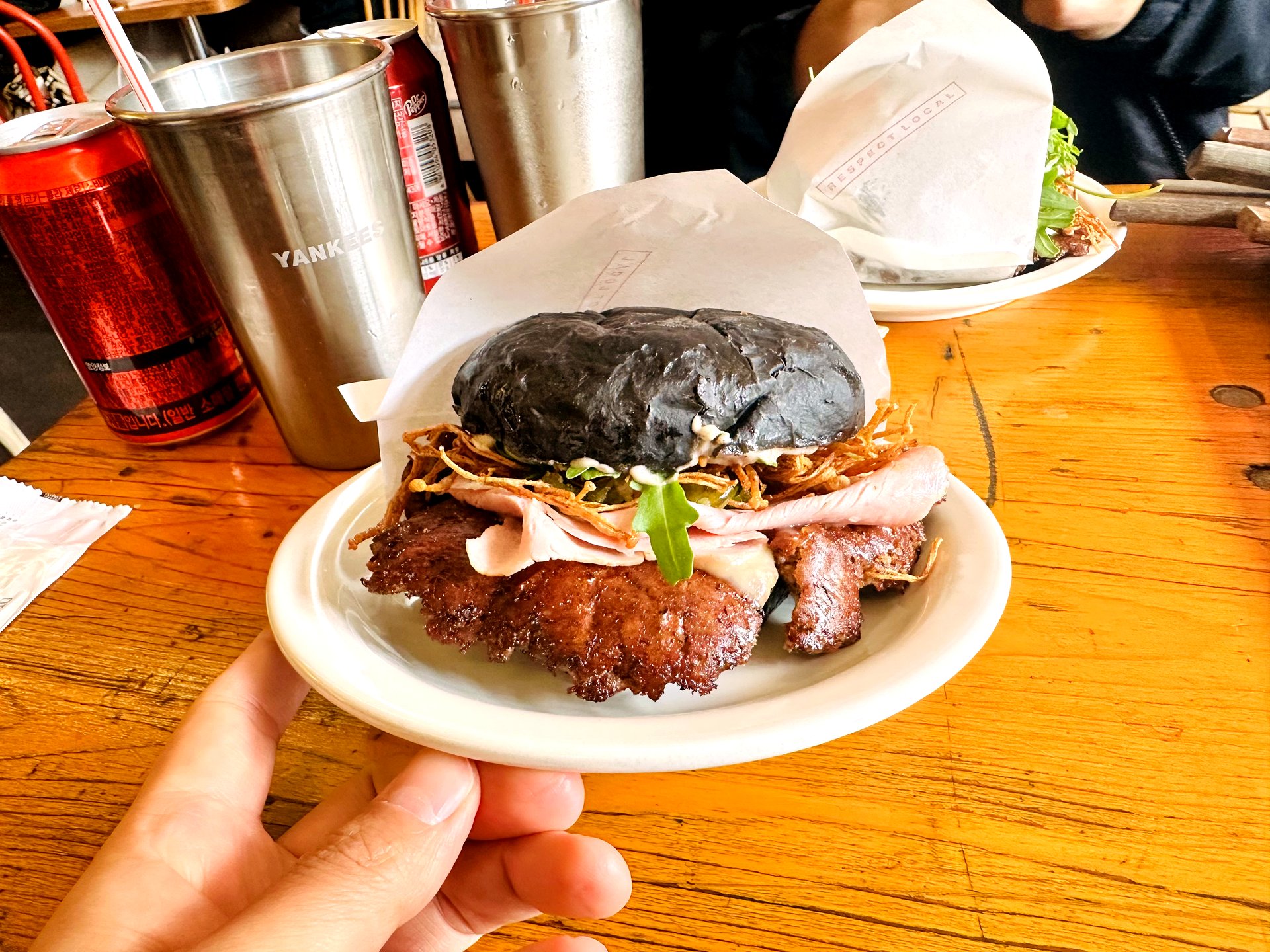 Mullae Burger held up close-up with charcoal black bun and fried enoki