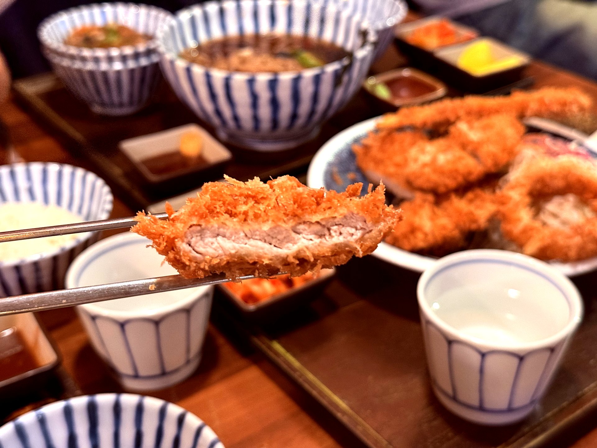 Crispy anshim donkkaseu held with chopsticks showing pink pork interior at Basak Jeju
