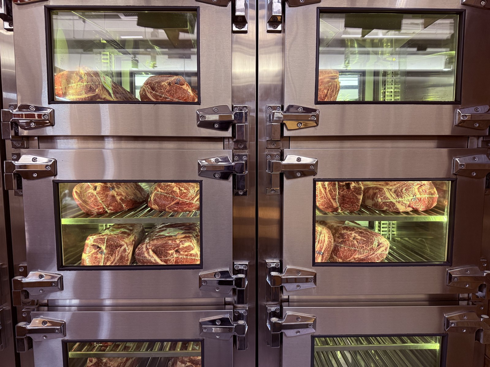 Stainless-steel dry-aging meat lockers with glass viewing panels showing hanging hanwoo ribeyes