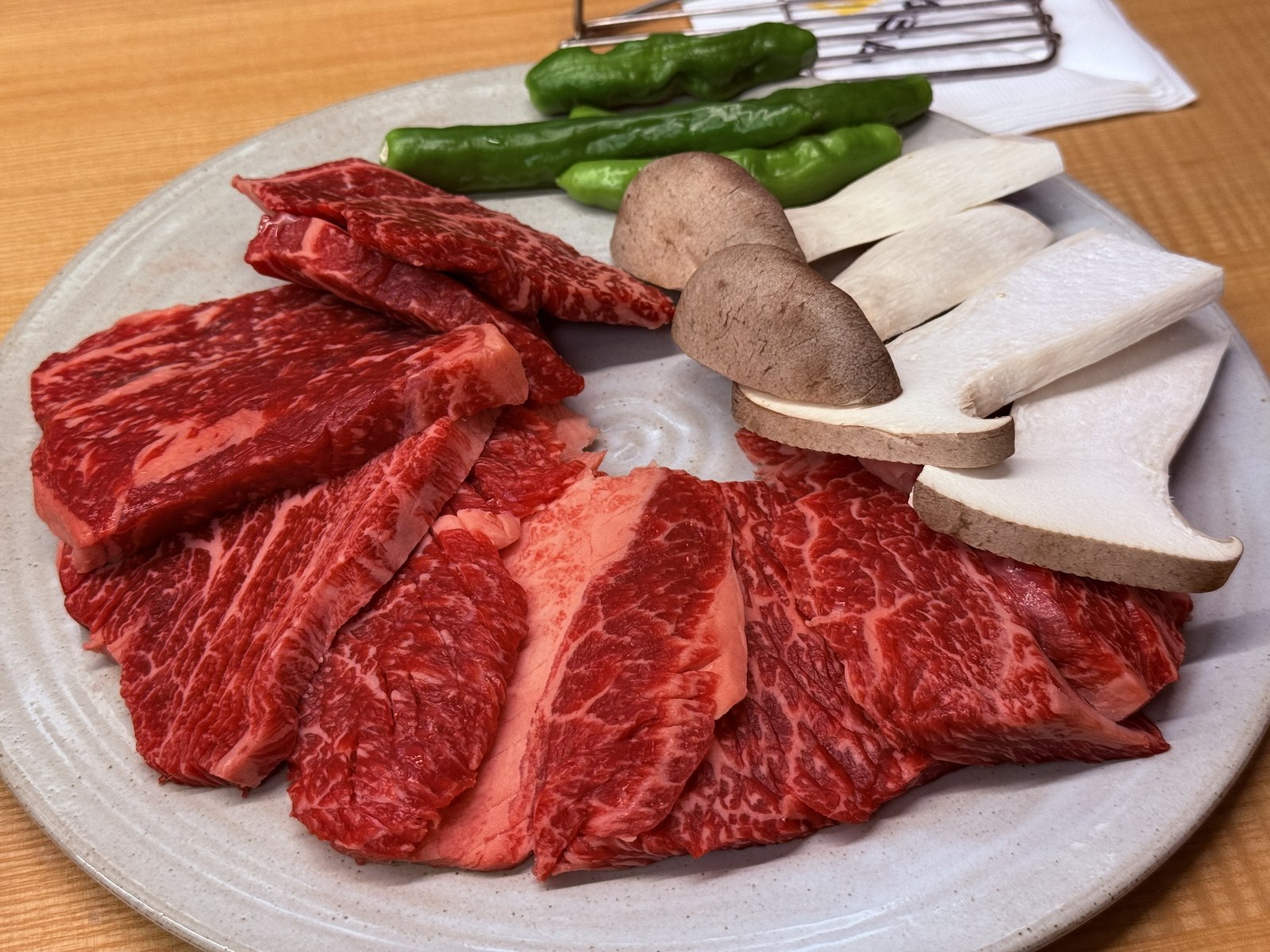 Hanwoo sirloin raw slices on white plate with shishito peppers and king oyster mushroom slices