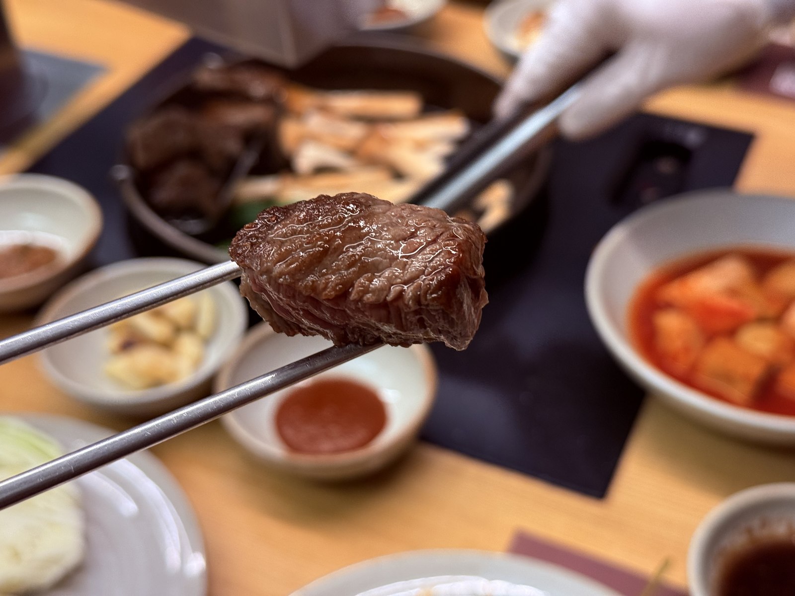 Single bite of grilled hanwoo sirloin held with chopsticks - mahogany crust visible, ruby interior