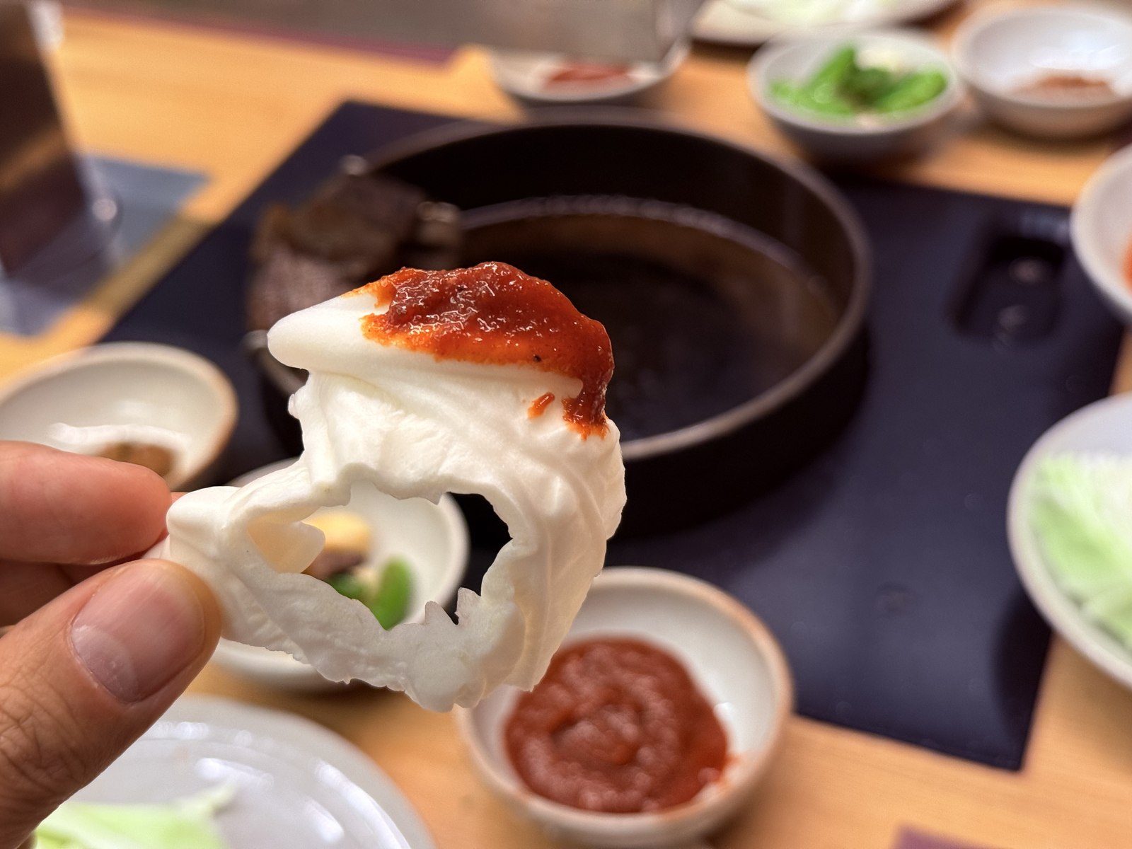 Cabbage leaf folded around grilled hanwoo with fresh red gochujang stripe visible - the signature Daedo move