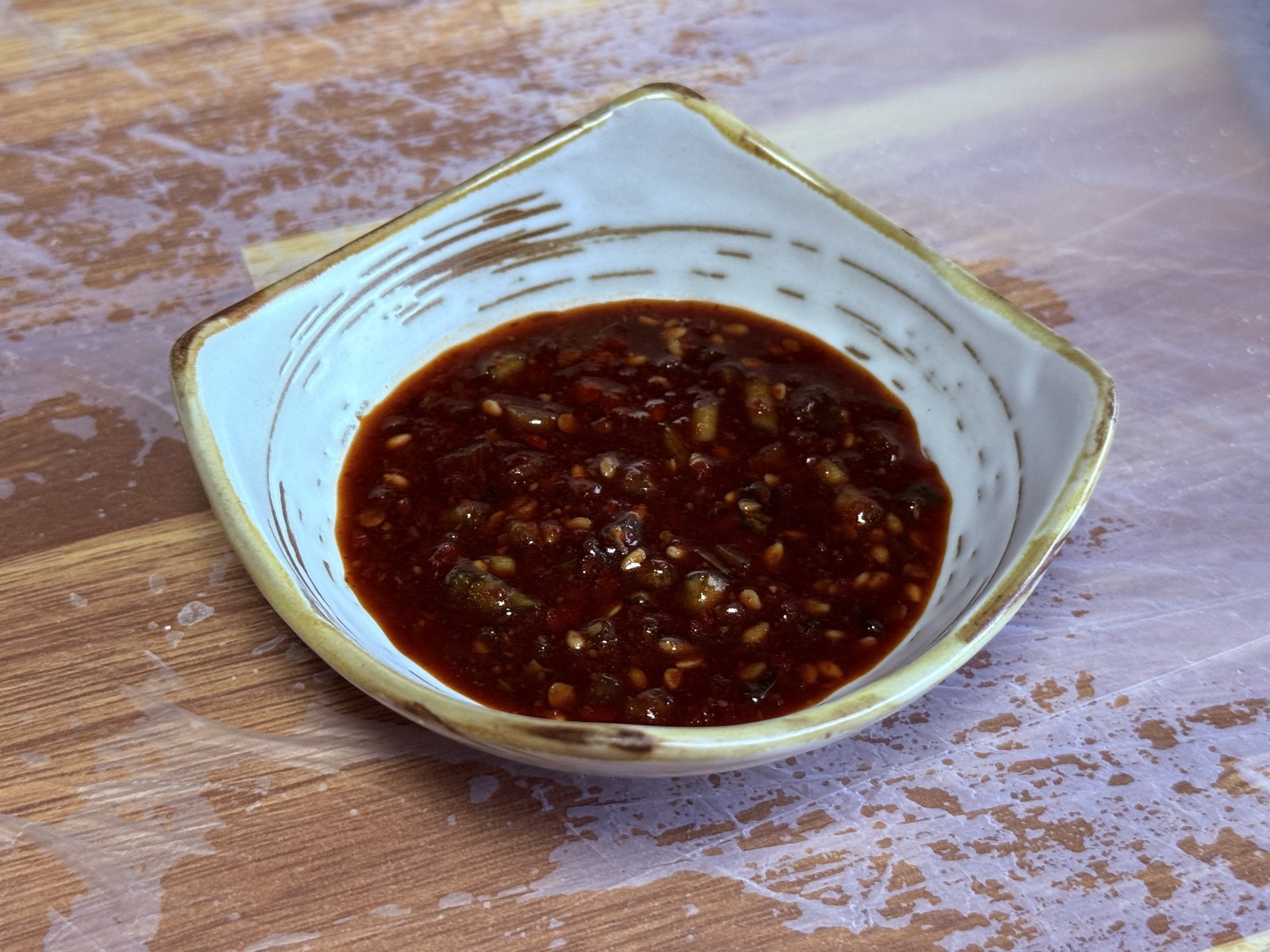 Close-up of the yangnyeom-ganjang dipping sauce at Eondeokwie Jangdokdae - dark soy-based sauce with red chili flakes, chopped garlic, sesame seeds, and green onion in a rustic ceramic dish