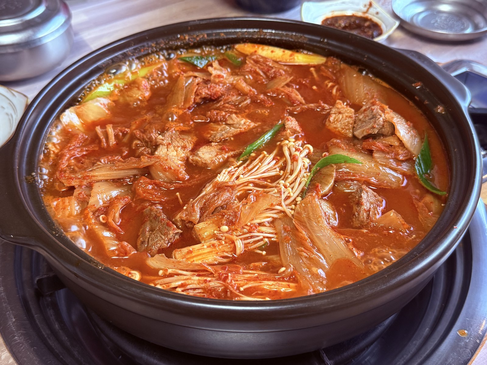 Eondeokwie Jangdokdae kimchi-jjim halfway through eating - pork shoulder now cut into chunks mixed with softened aged kimchi, enoki mushrooms, and chili broth in the black clay pot