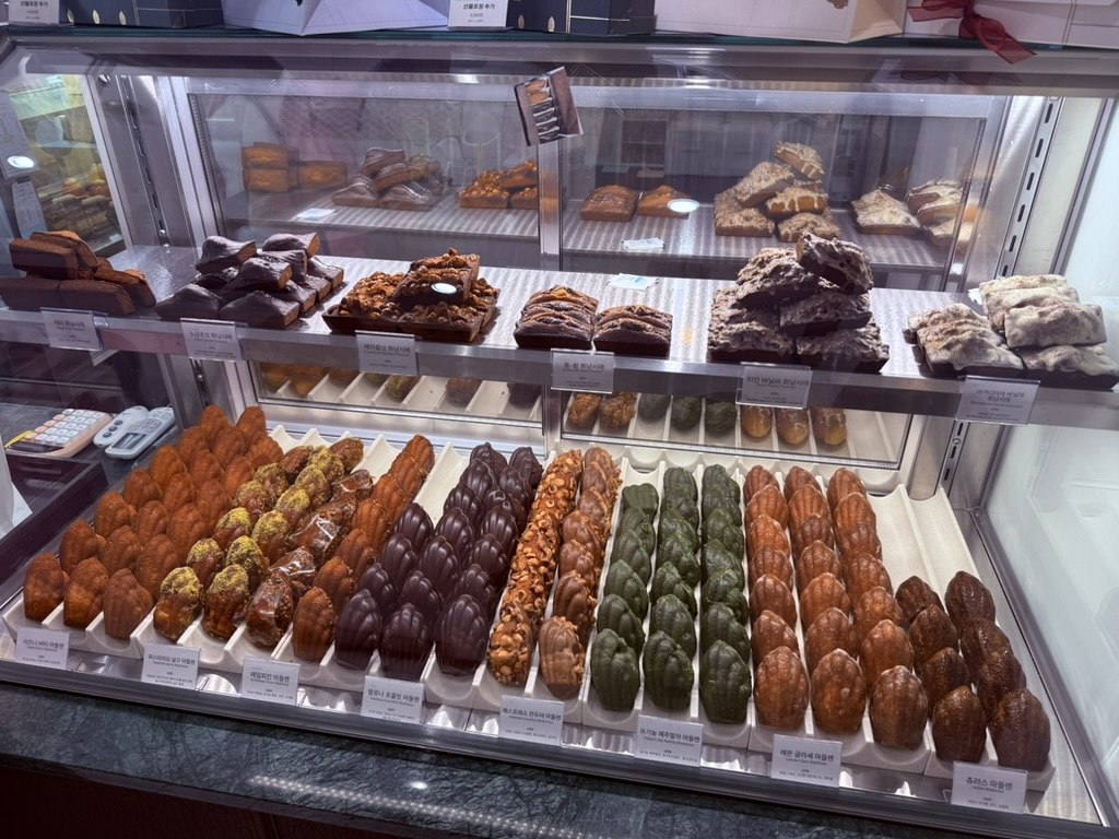 Display rack of Gwajabang madeleines - rows of lemon glacé, plain, chocolate-coated, hazelnut, matcha, cocoa flavors in shell shape