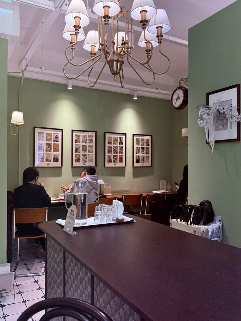 Gwajabang interior - sage-green walls, brass chandelier, framed photos on wall, seated customer at counter