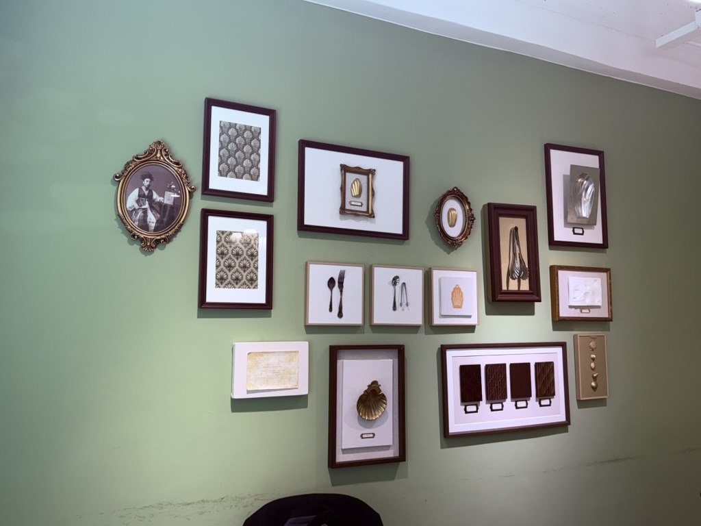 Gallery wall of small framed prints, photos and silver-spoon shadow-boxes on sage-green wall