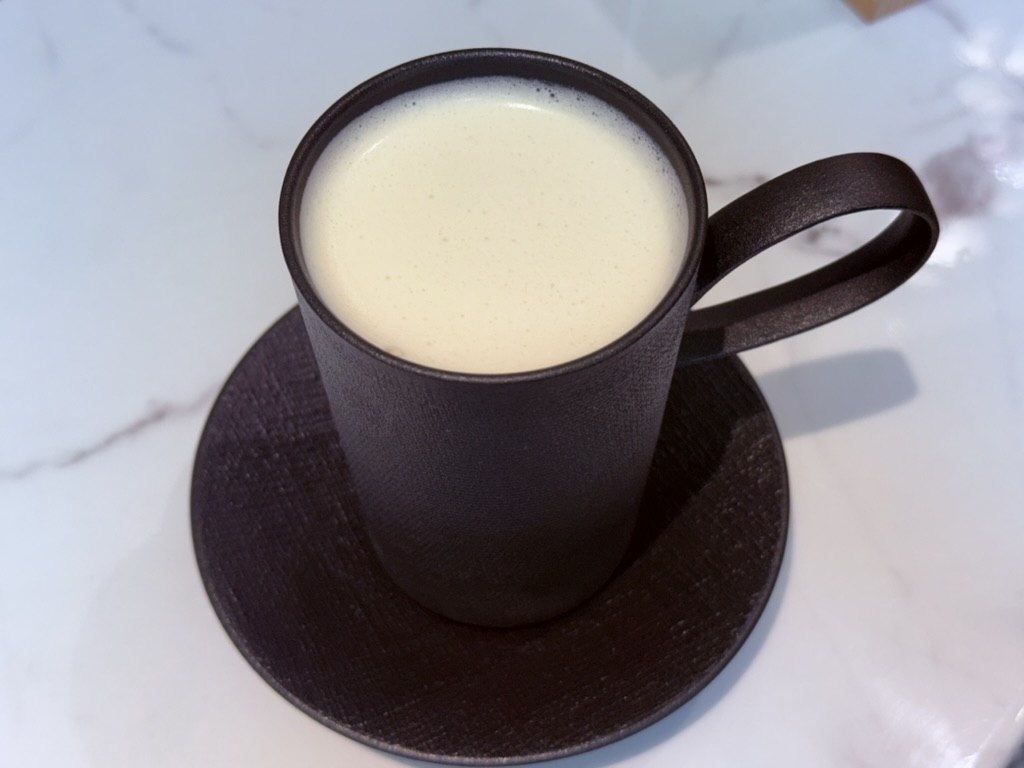 Gwajabang milk tea in dark black mug - creamy foamed surface, on white marble table