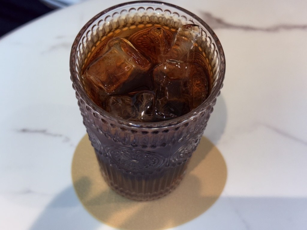 Iced Americano in faceted ribbed glass cup on white marble table - dark coffee with ice cubes