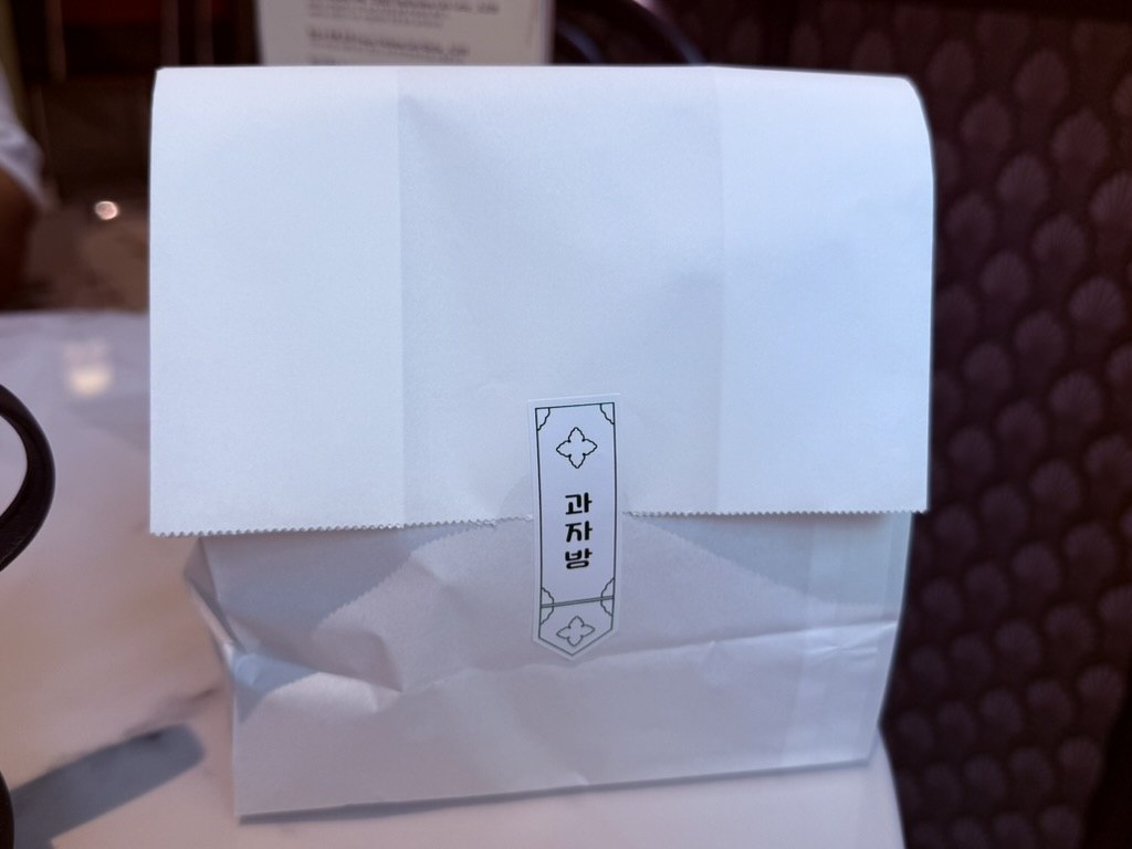 Gwajabang takeout paper bag - white kraft paper with Korean logo sticker, on dark surface