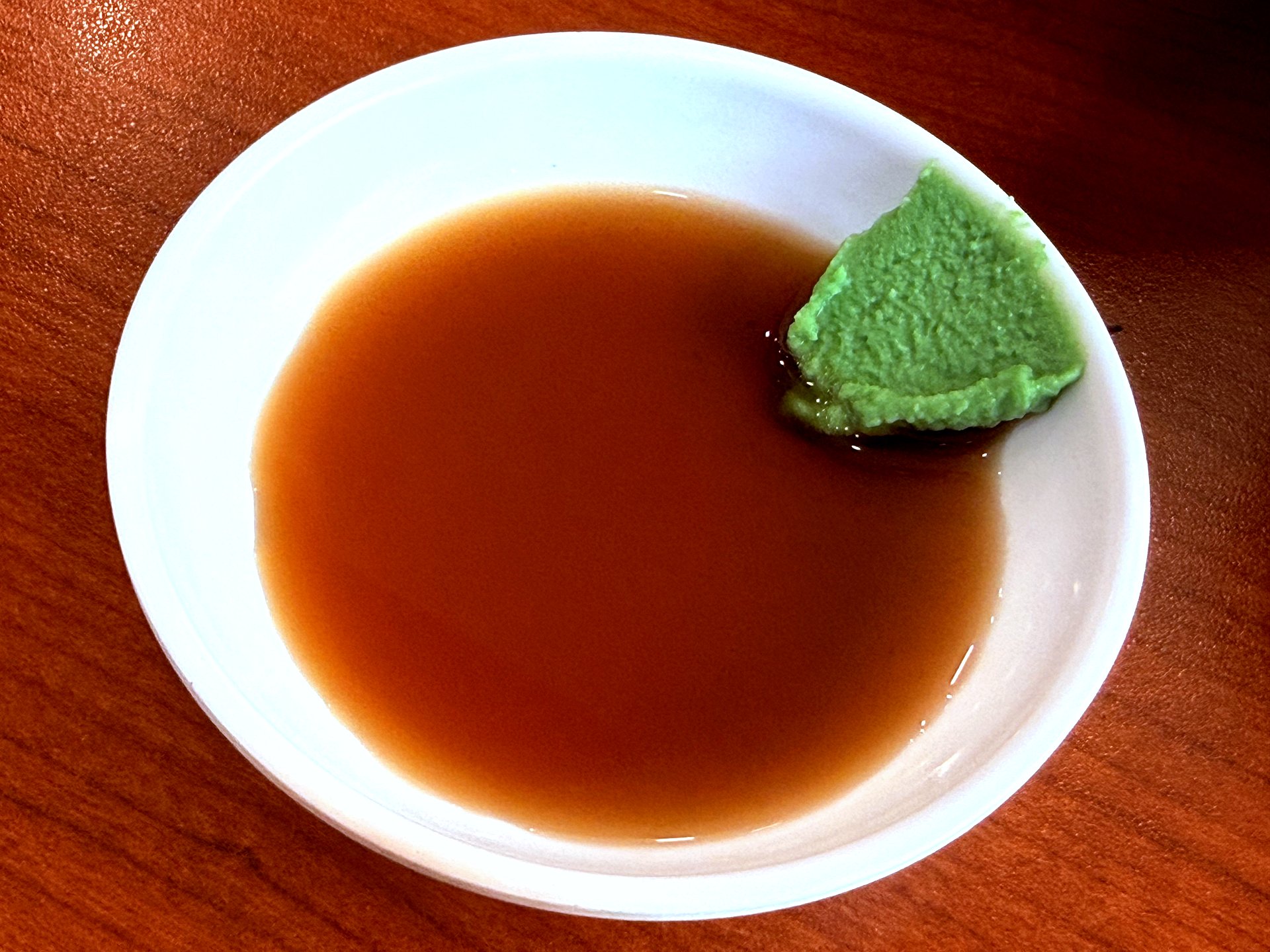 Small white bowl with brown soy sauce and a generous wedge of green wasabi paste