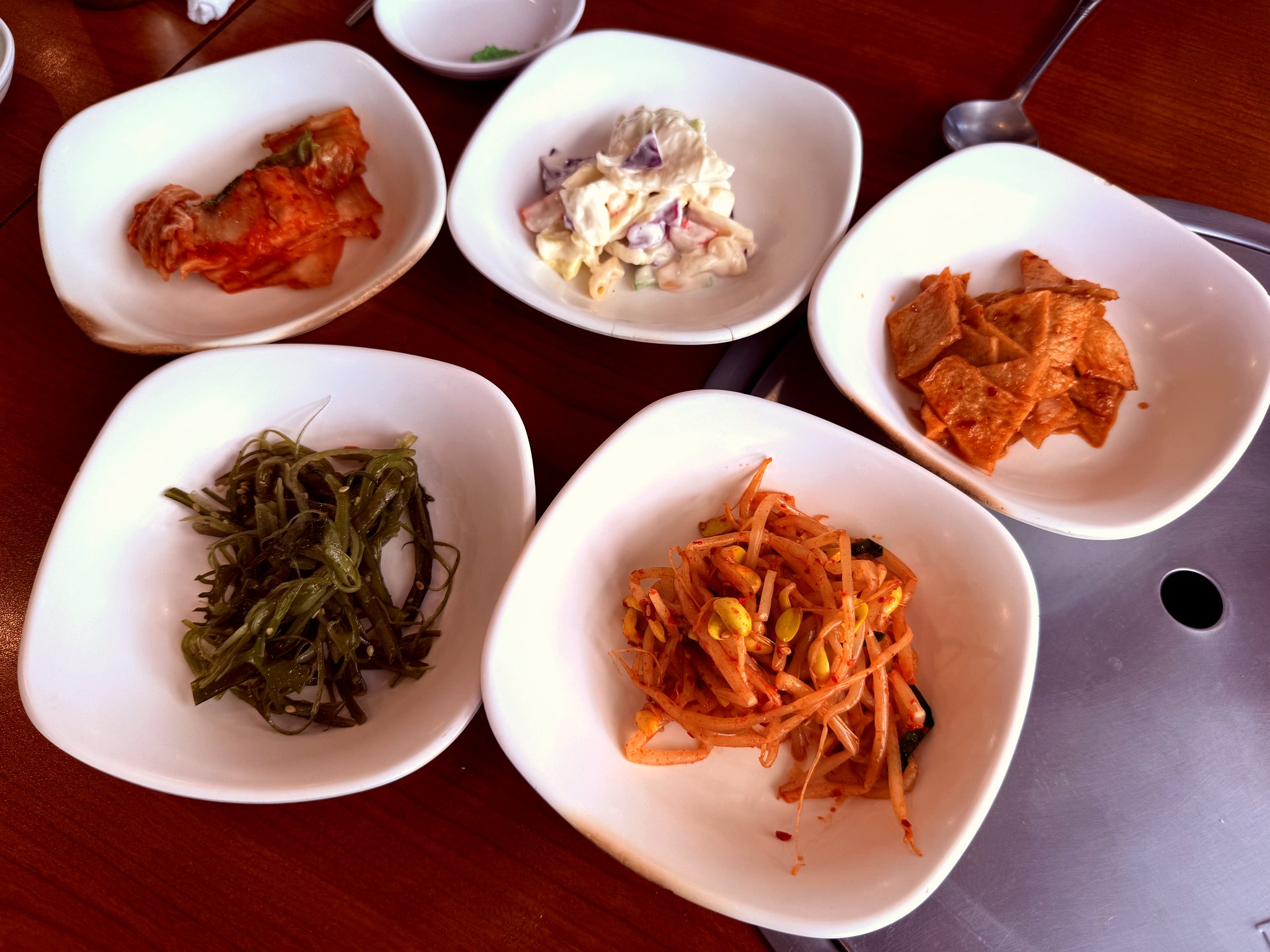 Five small dishes of banchan - kimchi, potato salad, pickled radish, seaweed, sprouts