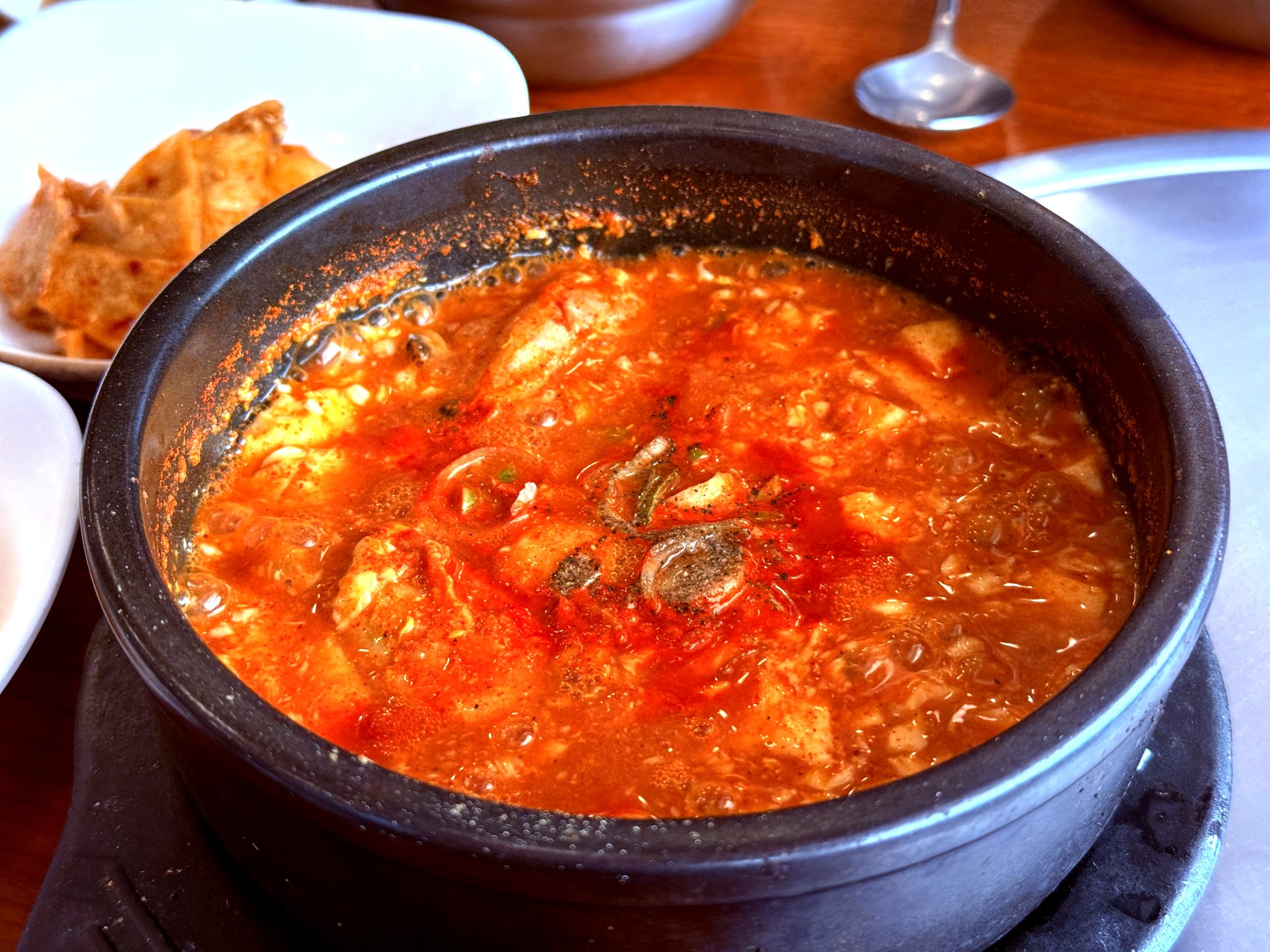 Spicy soft tofu stew in a dark stone pot, bright red broth with tofu chunks visible