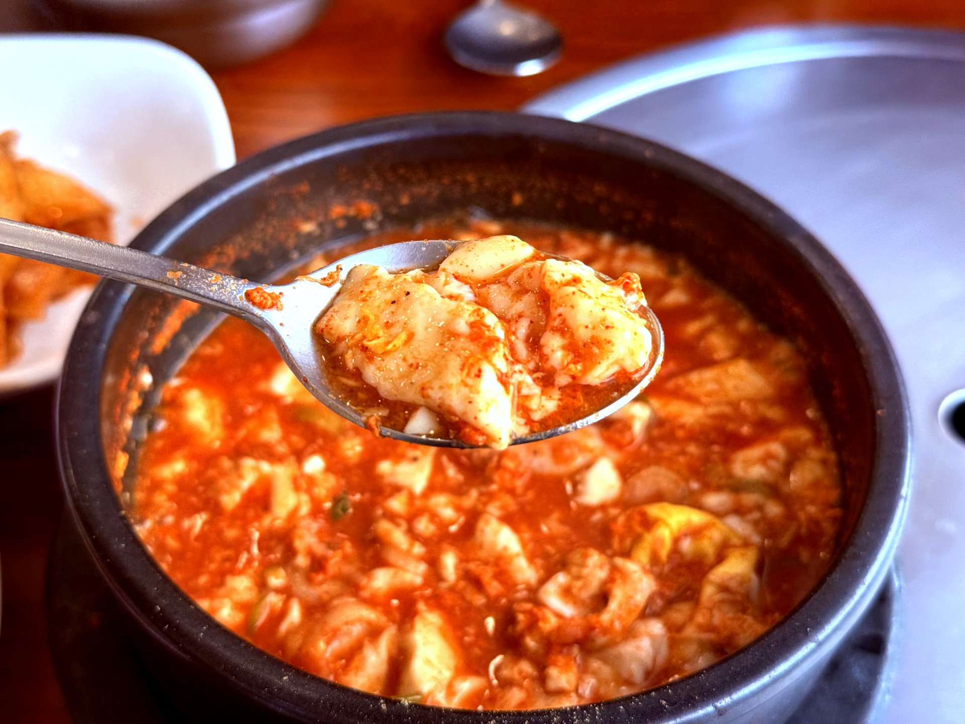Spoonful of silky soft tofu lifted from the red broth