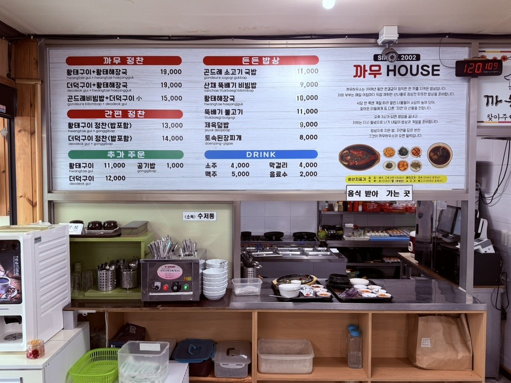 Kkamu House menu board - Korean menu listing 황태구이 hwangtae-gui sets at 19000 won and other baekban dishes, on the wall above the self-service food pickup counter