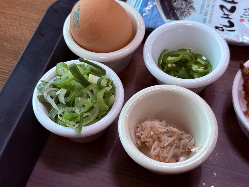 Customization tray at Kkamu House - small bowls of sliced green onion, sliced jalapeño, chopped saewujeot (fermented shrimp), and a whole brown egg in a ceramic cup