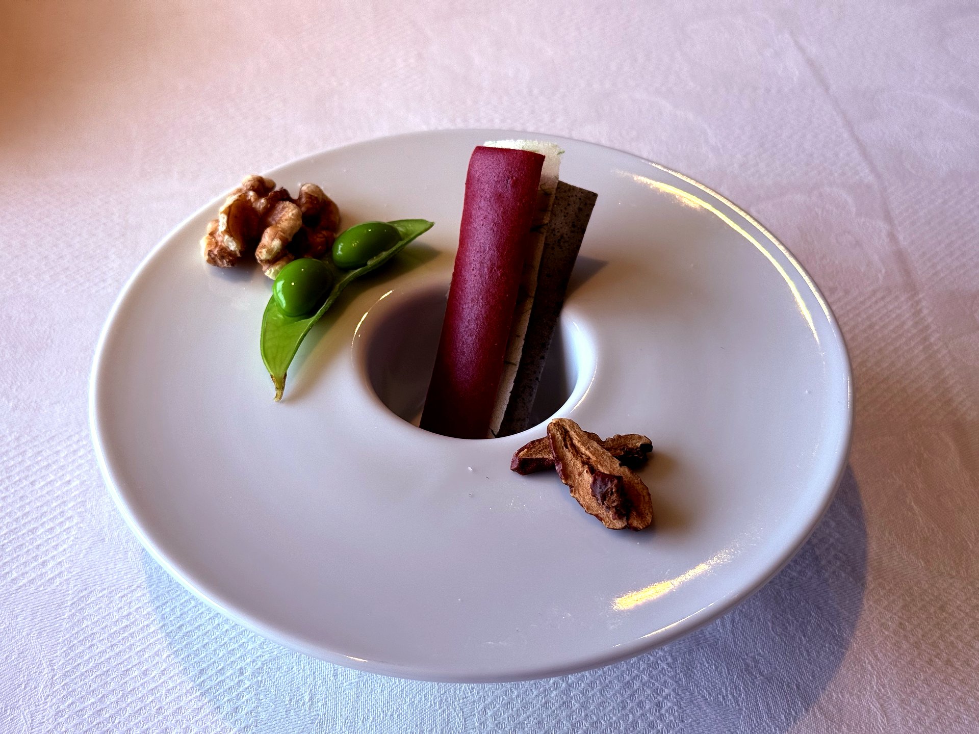 Welcome amuse - walnut, edamame puree, fruit roll, and tea leaf on white plate