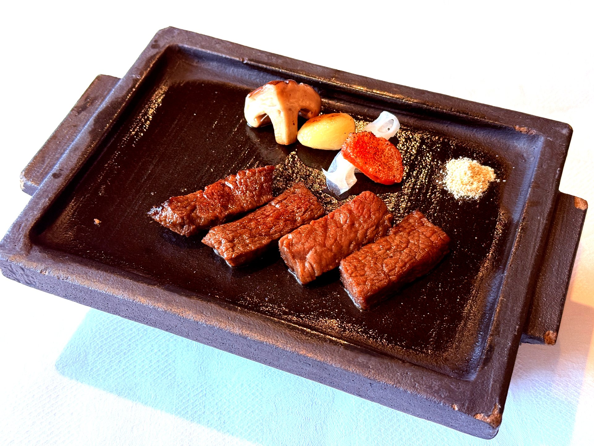 Four medallions of grilled Hanwoo tenderloin on hot stone with garlic, persimmon, salt