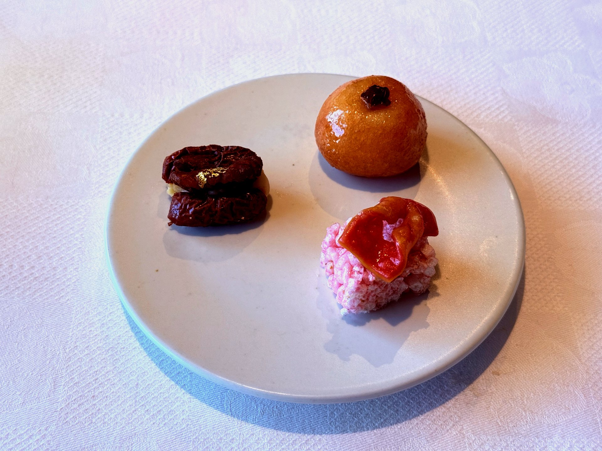 Three confections - sweet rice puffs with red glaze, golden honey bun, and fig sandwich with gold leaf