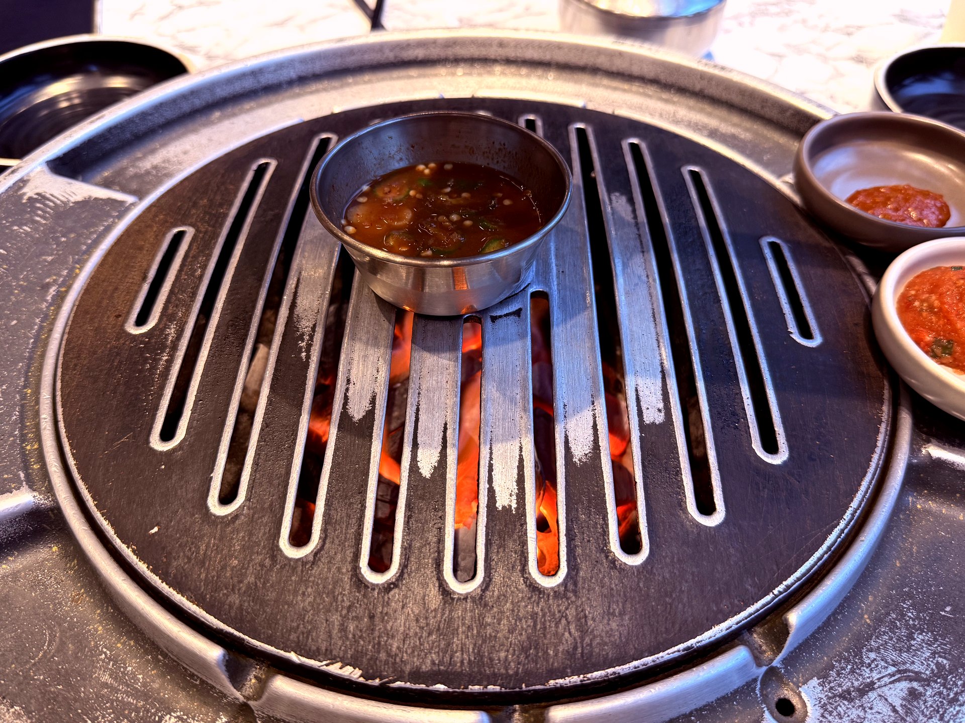 Charcoal grill with glowing coals and a small bowl of sauce