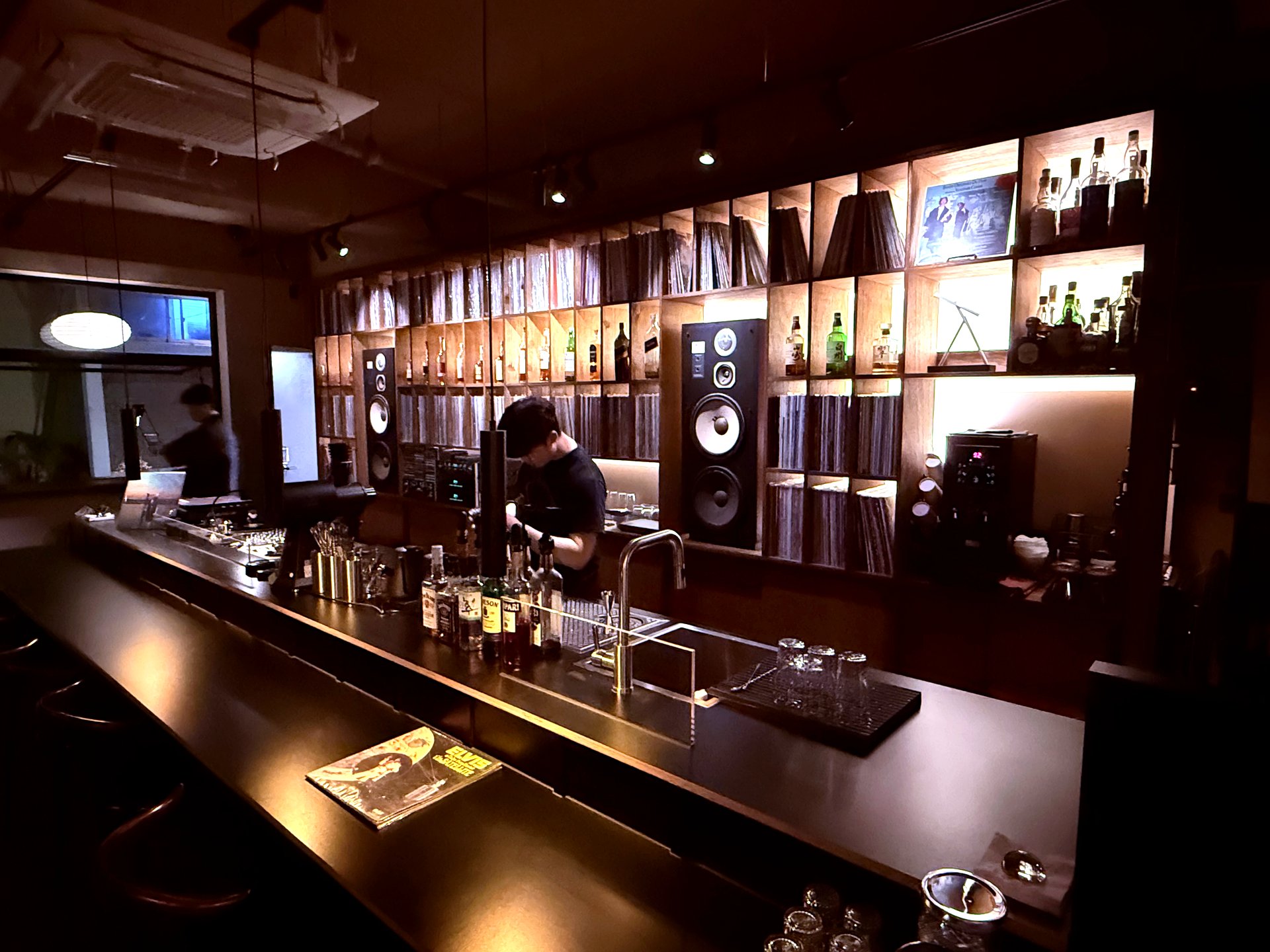 Bartender at the bar, JBL speakers and LP wall behind