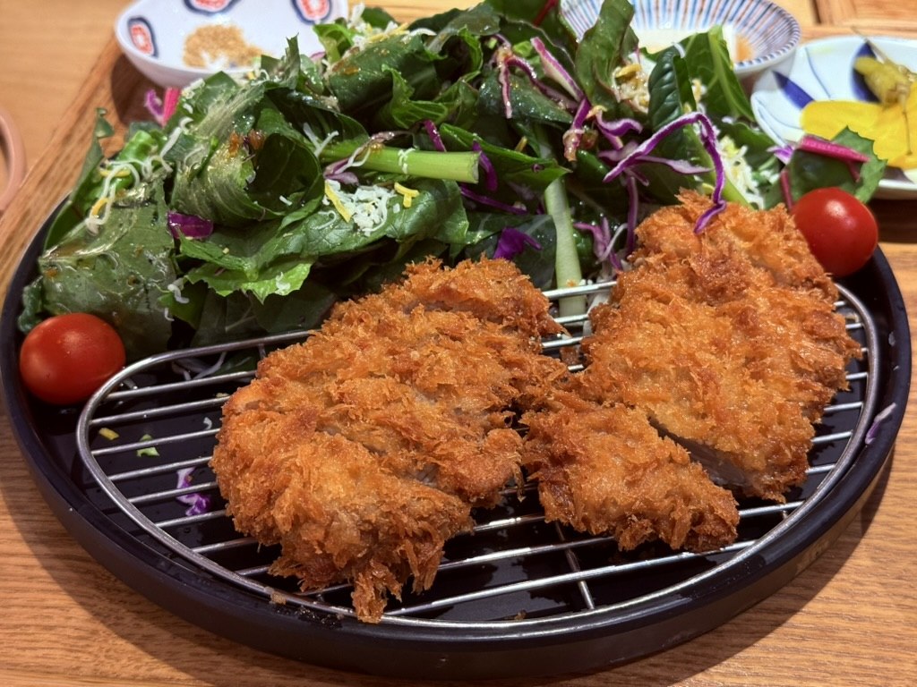 Close-up of Bueongi Donkatsu salad-donkatsu - shatter-crisp panko-breaded pork cutlet pieces on a wire rack with cherry tomato and a giant mound of fresh mixed greens and red cabbage