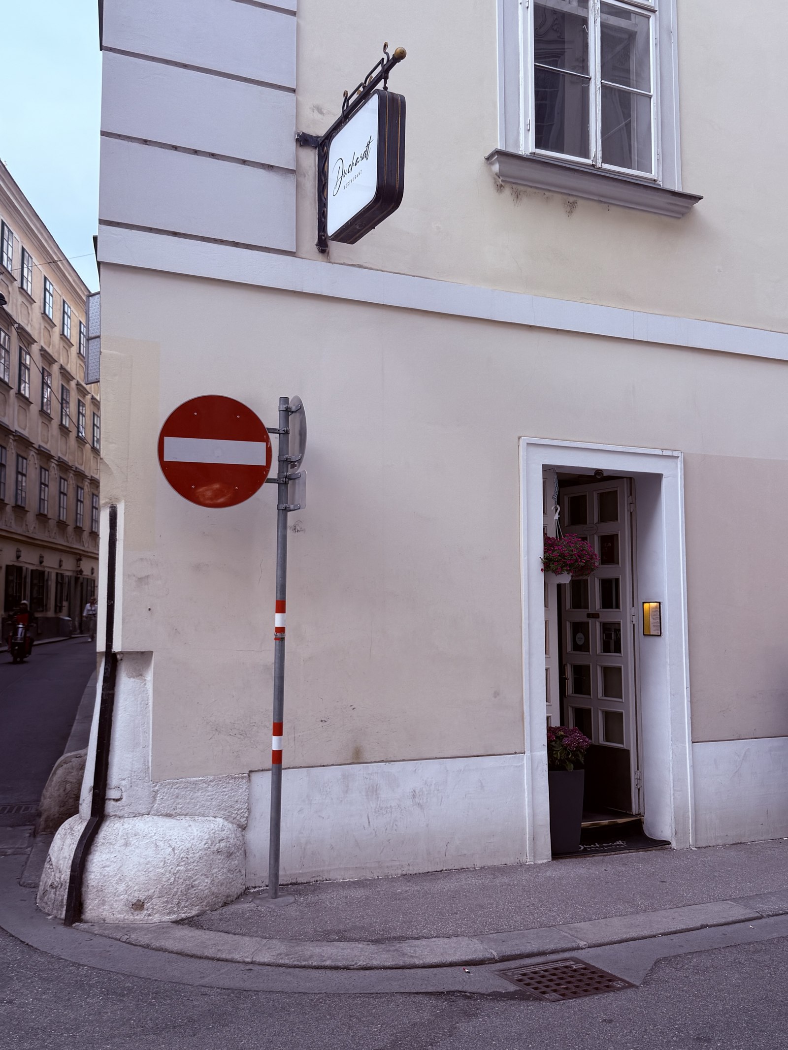 Restaurant Duchardt exterior - corner of a quiet Vienna Inner Stadt street with a small black blade sign with Duchardt calligraphy on the wall above an understated entrance, classic Vienna cream-colored building facade, narrow medieval side street