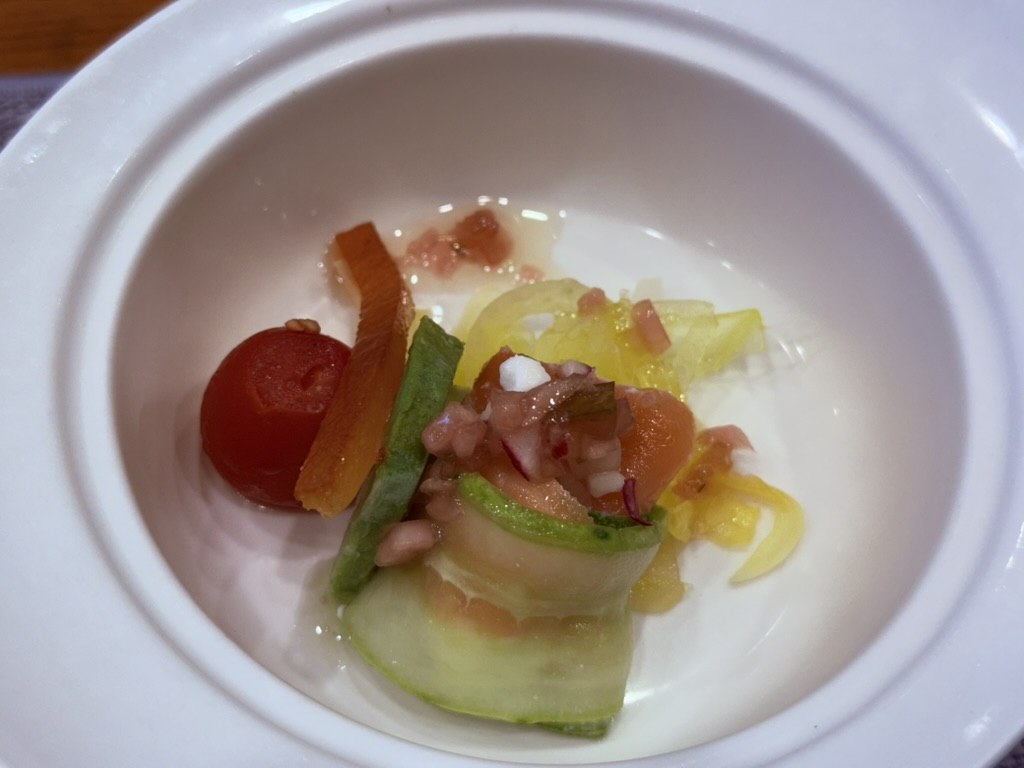 Naedang first course amuse - small white bowl with poached cherry tomato, julienned cucumber and yellow paprika cylinder, diced tomato and apple salsa garnish, on a cream tablecloth