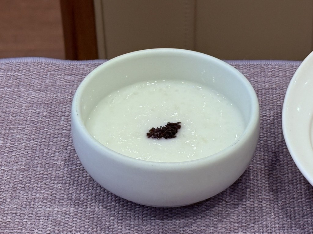 Naedang tarakjuk milk porridge with morel mushrooms - small white bowl of silky ivory rice-and-milk porridge with diced black morel mushroom and fermented black bean reduction in the center