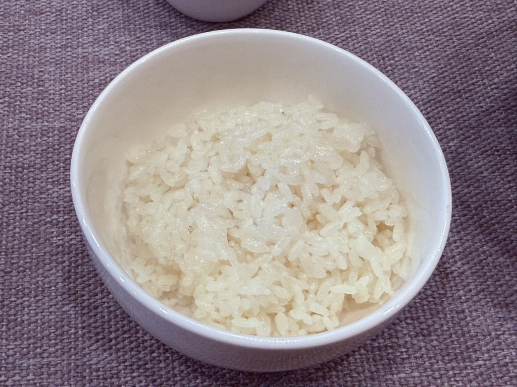 Small white bowl of Korean short-grain steamed rice at Naedang - glossy white rice grains shaped into a small mound, sitting on a lavender linen tablecloth