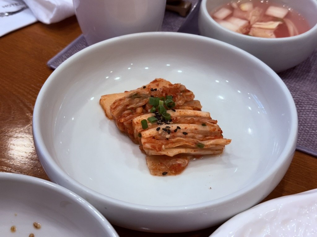 Naedang house-made cabbage kimchi close-up - small portion of finely chopped Korean napa cabbage kimchi with red chili paste, sesame seeds and green onion garnish, in a small round white bowl
