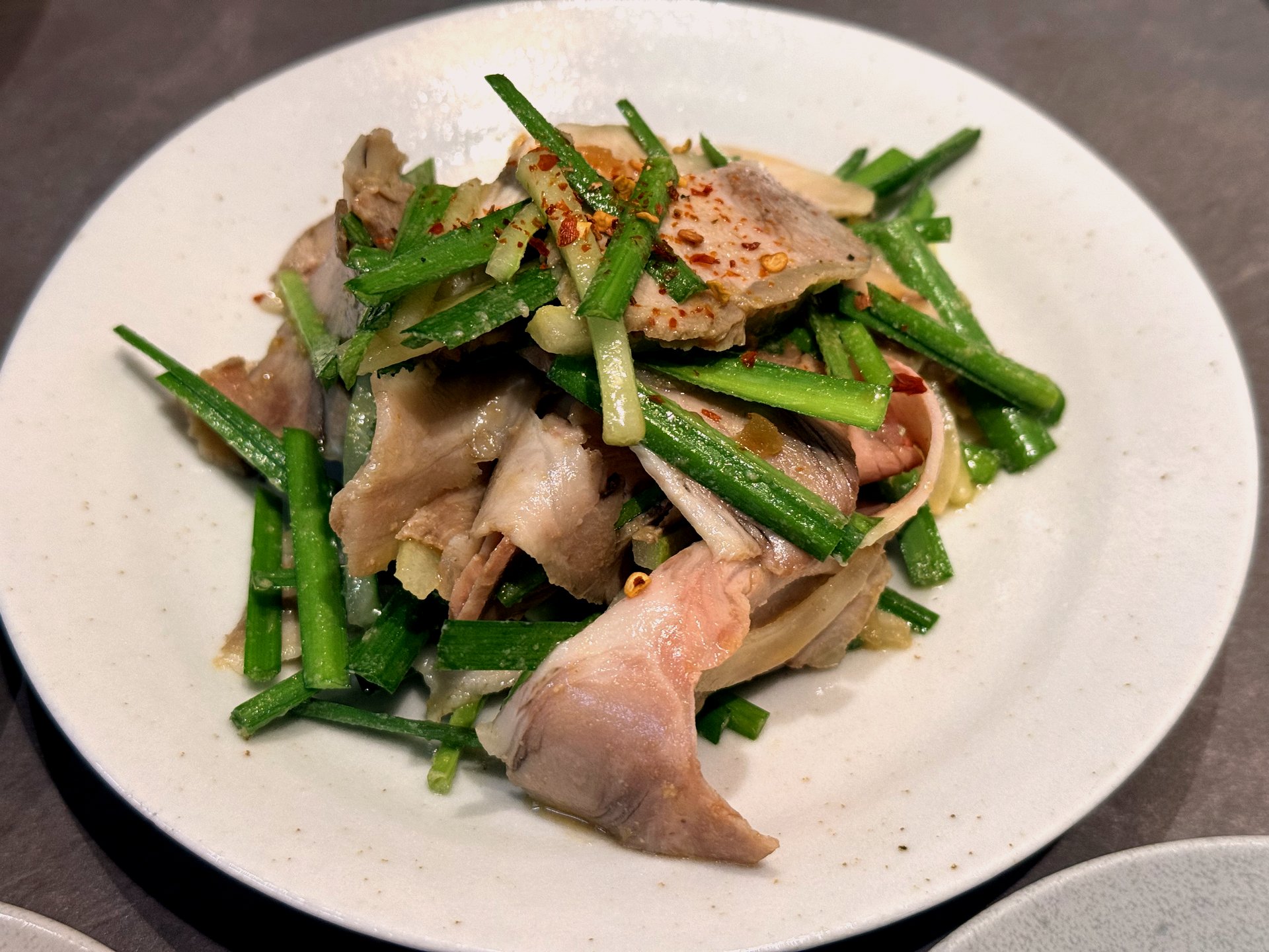 Jambong suyuk at Hyemindang Yongsan - a white plate of thin, slightly thick slices of torched cold pork belly and shoulder tossed with fresh garlic chives, thin cucumber, and a sprinkle of red chili flakes, the pork edges lightly charred from a torch