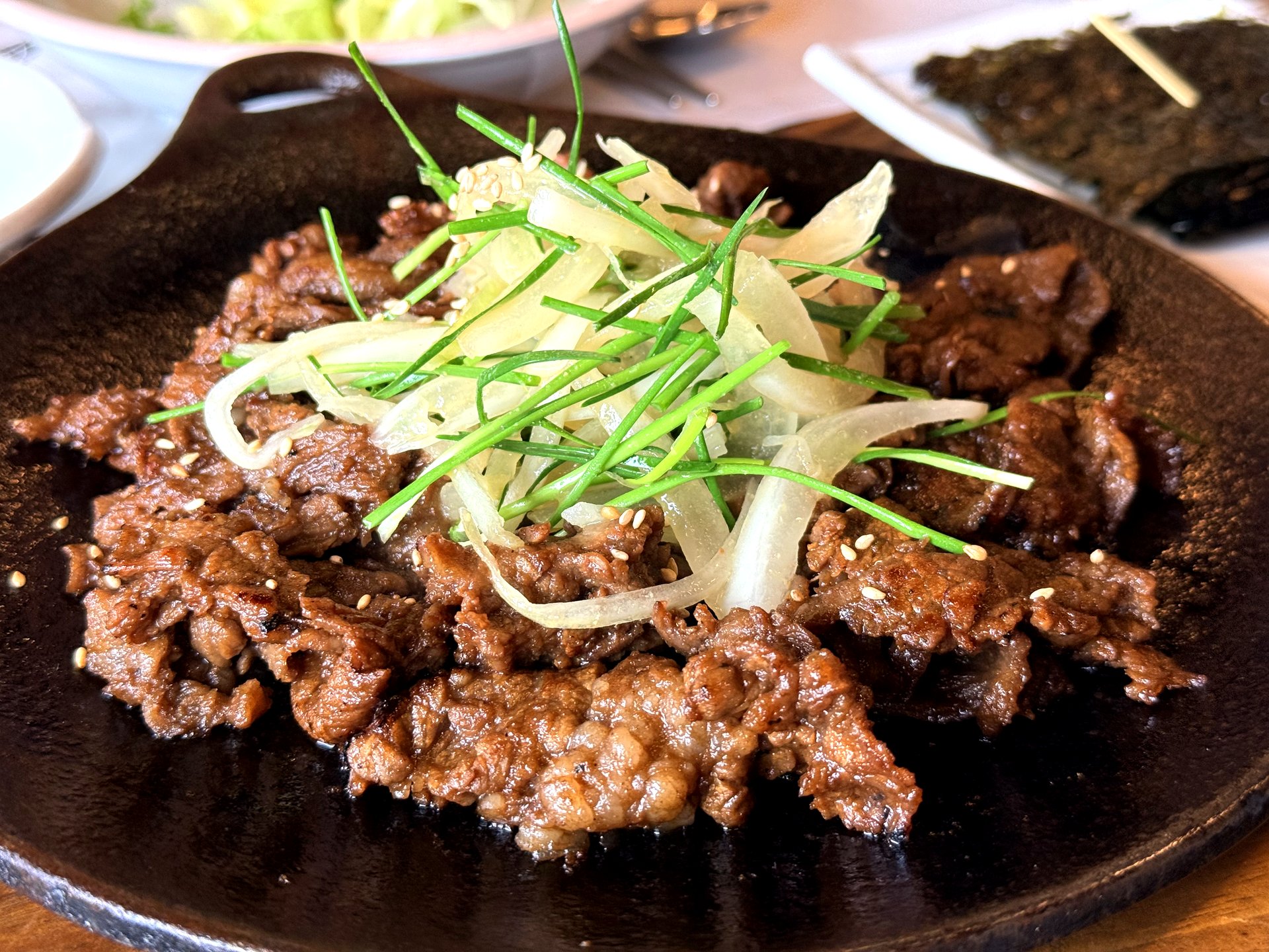 Haenuri Dongsan Deulbap 직화 바싹불고기 (dry-grilled bulgogi) - thin slices of caramelized soy-marinated beef cooked firm and glossy on a black cast-iron plate, topped with slivered white onion, green chive and sesame seeds