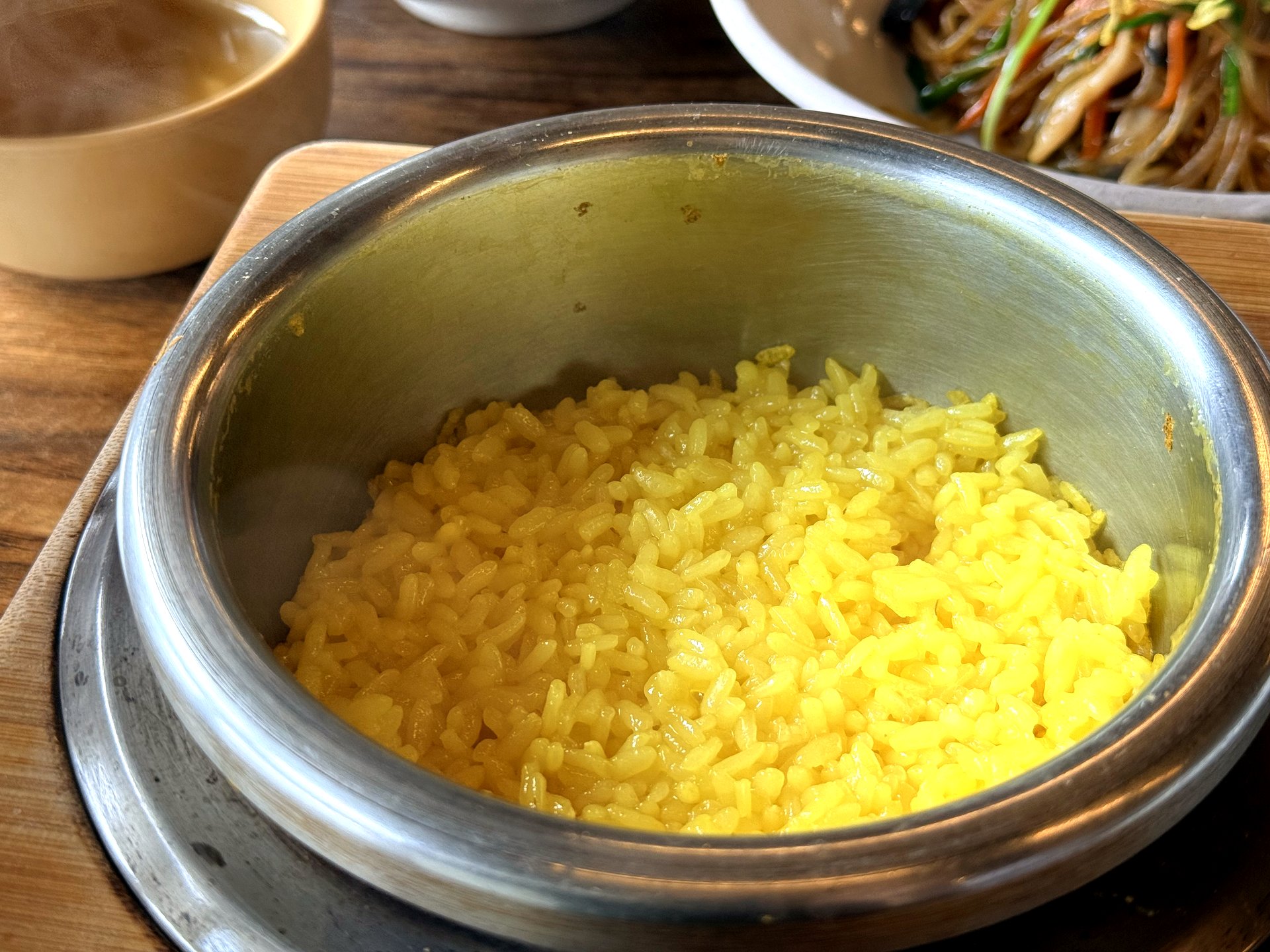Haenuri Dongsan Deulbap 강황밥 (turmeric rice) - a bowl of glossy bright yellow turmeric-tinted steamed rice in a stainless-steel bowl, part of the Korean set meal