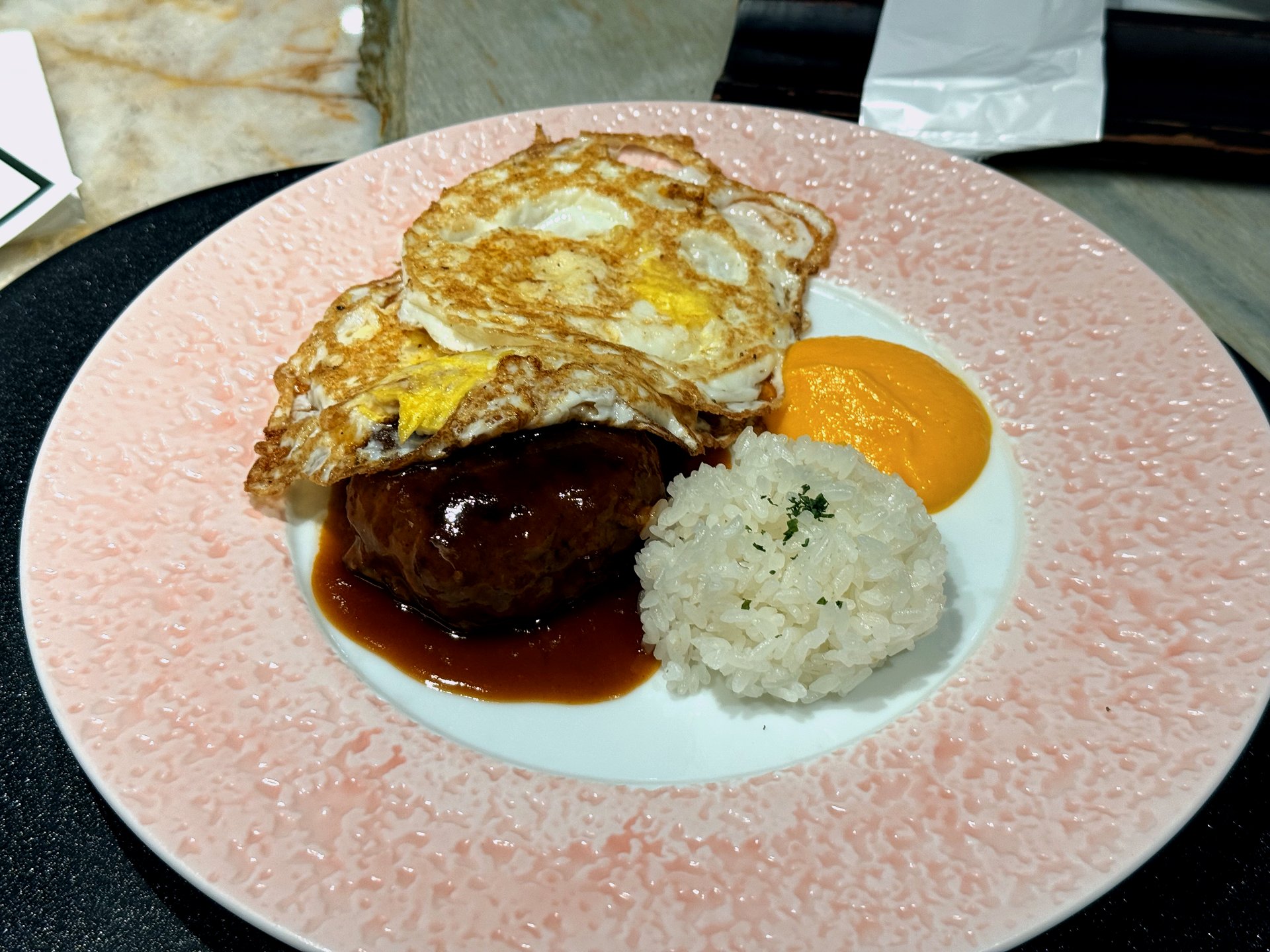 The kids set at Kawabe Teppanyaki Seoul - a pink-rimmed plate with a glossy hamburg steak (함박스테이크) in brown gravy, two fried eggs on top, a mound of white rice, and a swoosh of orange sauce