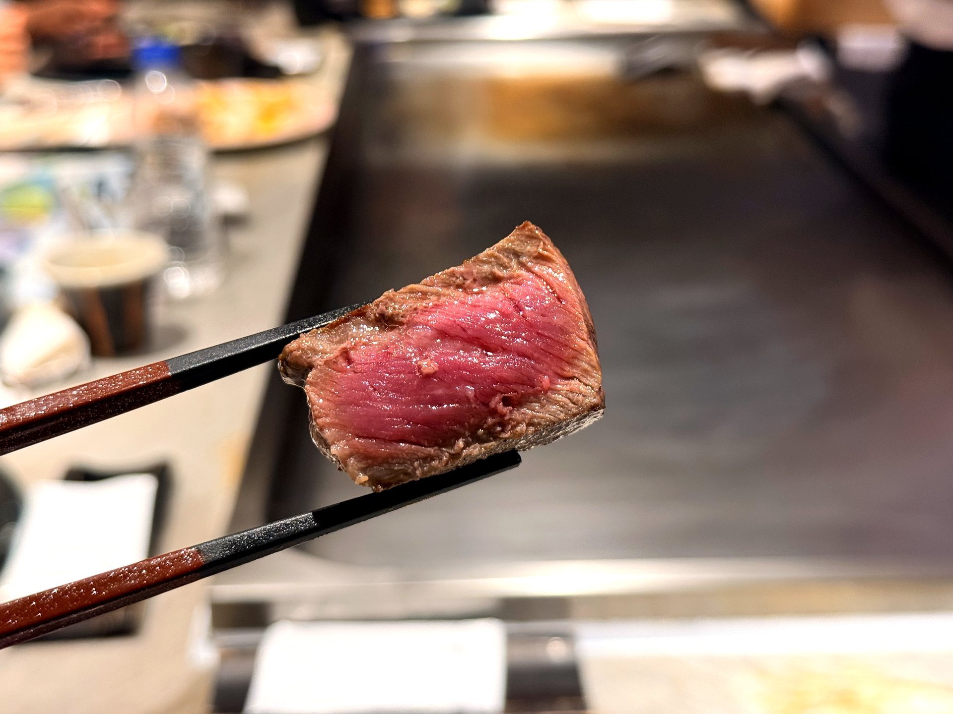 Close-up of a Hanwoo 1++ steak slice at Kawabe Teppanyaki Seoul - a single thick piece of seared Korean beef lifted in chopsticks, showing the seared crust and juicy rosy-pink medium-rare interior
