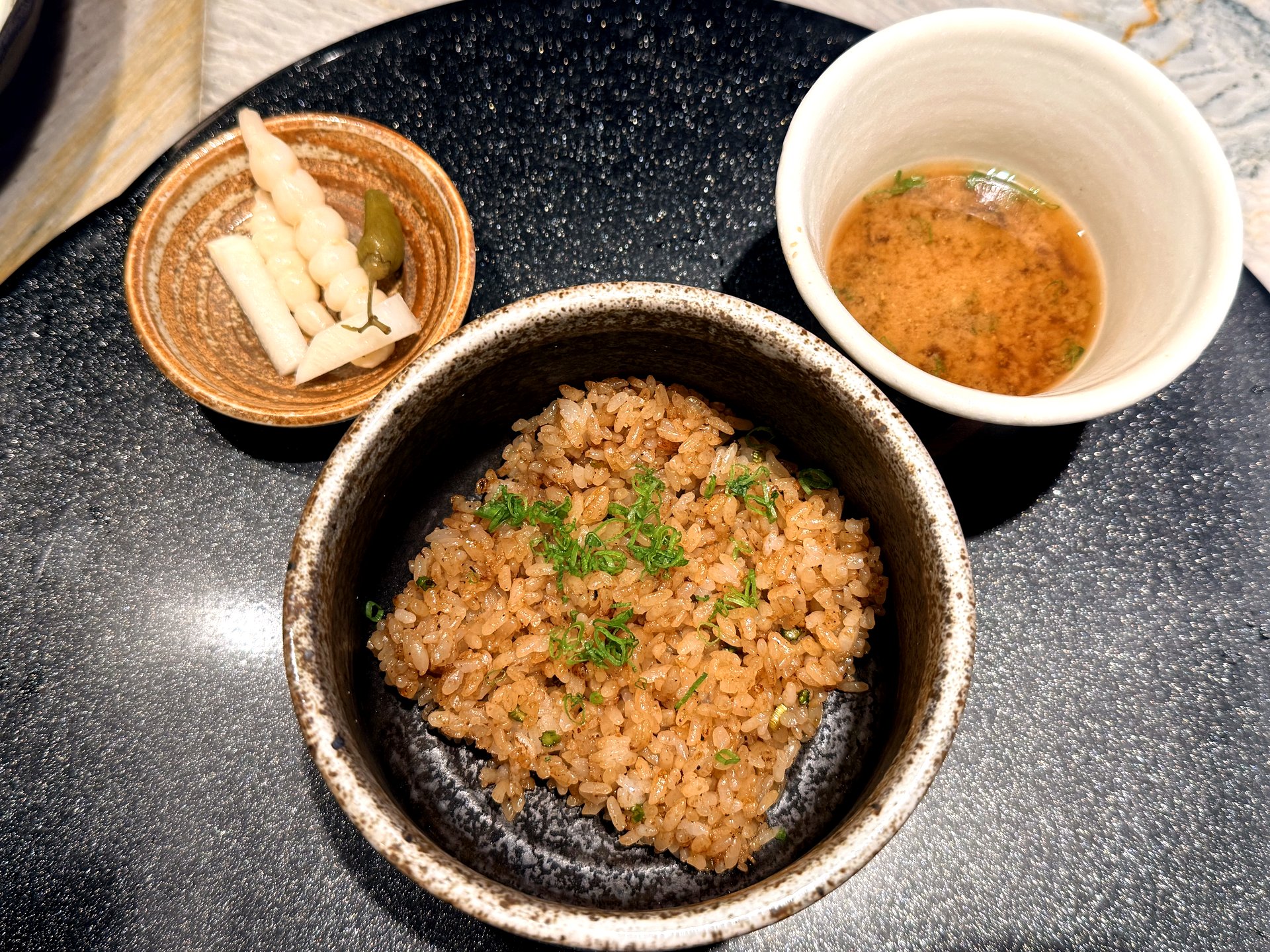 Course seven at Kawabe Teppanyaki Seoul - a bowl of glossy soy-seasoned garlic fried rice topped with chopped scallion, served with a small dish of pickles and a cup of clear soup
