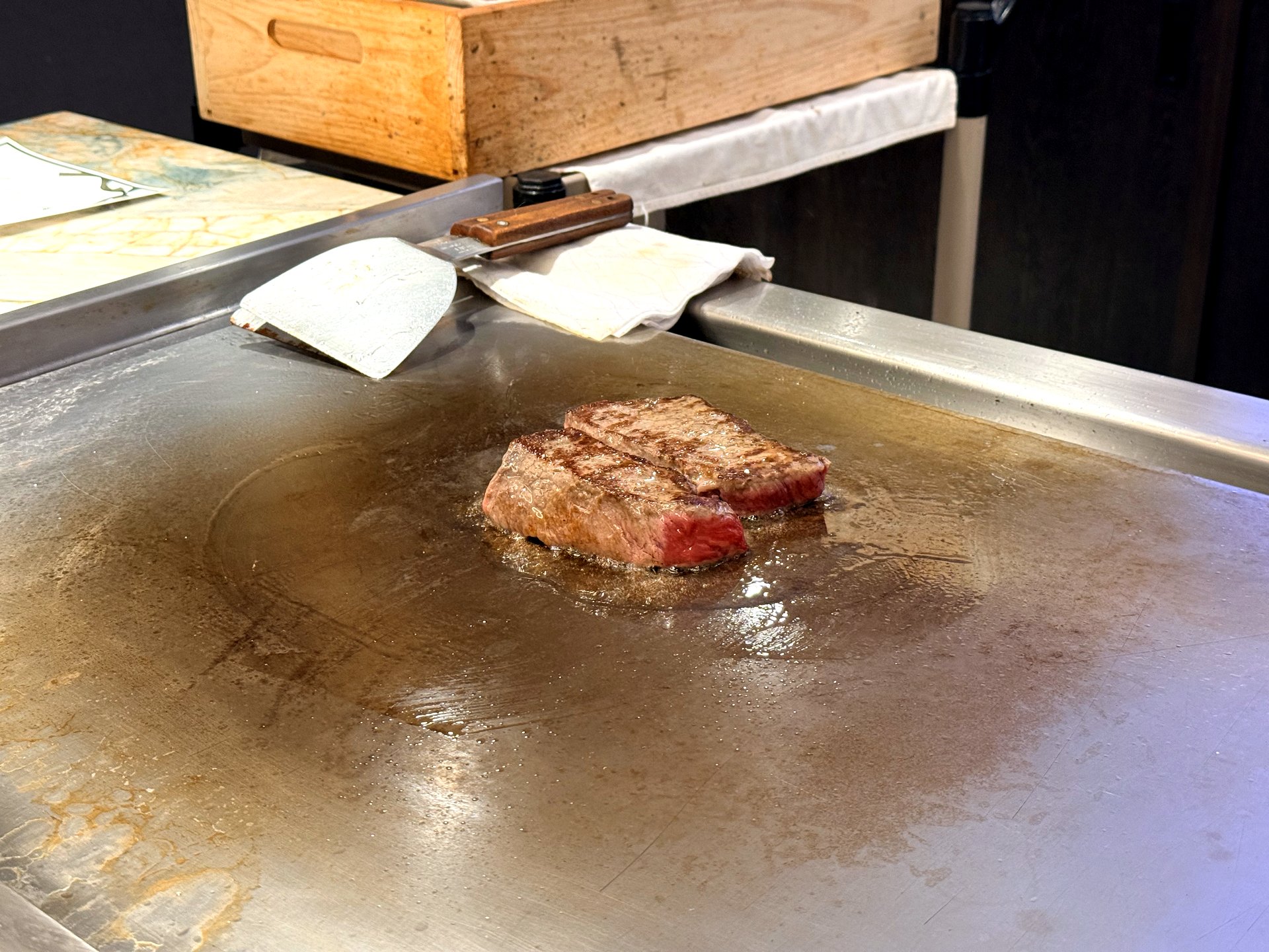 A Hanwoo 1++ ribeye steak searing on the hot teppanyaki griddle at Kawabe Teppanyaki Seoul, two thick well-marbled Korean beef steaks with grill marks browning in their own fat