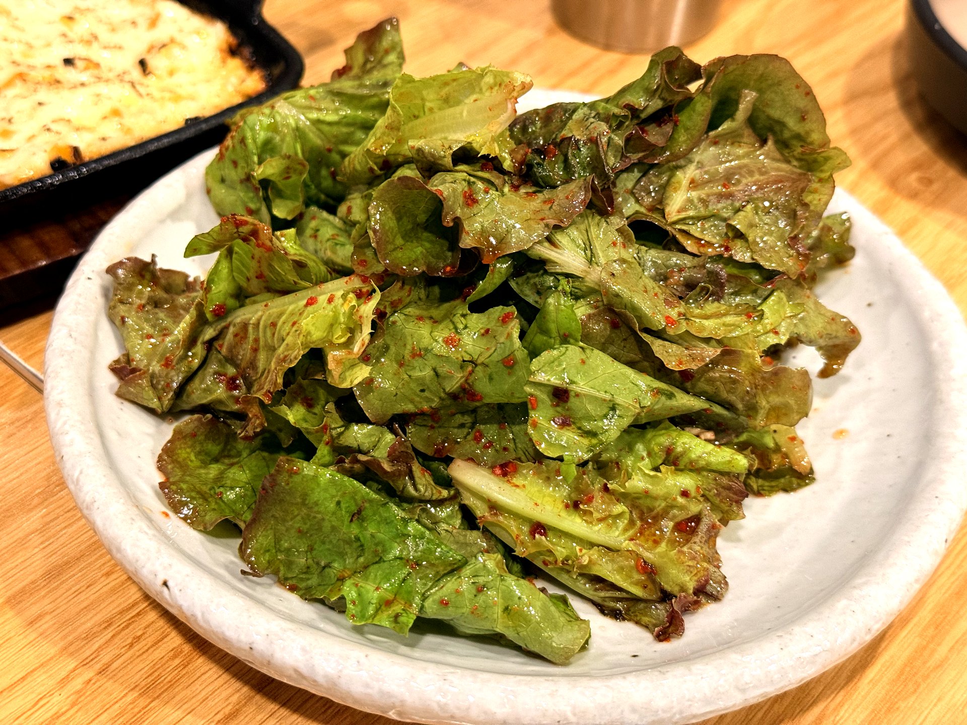 Oso Galbi 상추무침 (seasoned lettuce salad) - a mound of fresh red-leaf and green lettuce tossed in a glistening red gochugaru-and-sesame-oil dressing, on a white ceramic plate, a banchan at a Korean BBQ restaurant
