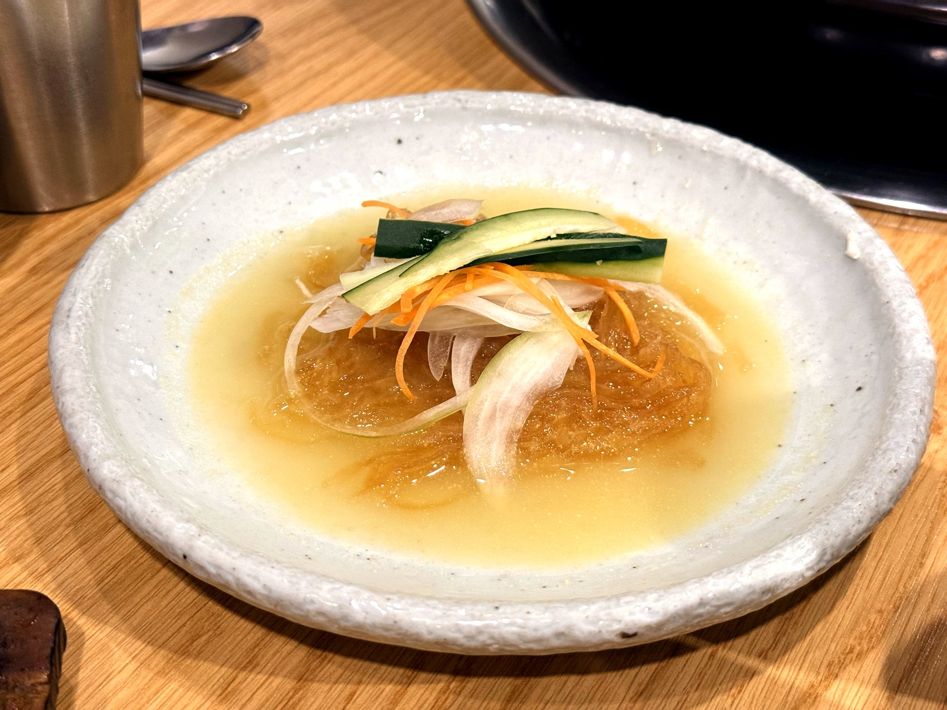 Oso Galbi 해파리냉채 (chilled jellyfish salad) - translucent jellyfish strands with thinly sliced onion, cucumber and carrot in a light tangy pale broth, on a white ceramic plate, a refined banchan at a Korean BBQ restaurant