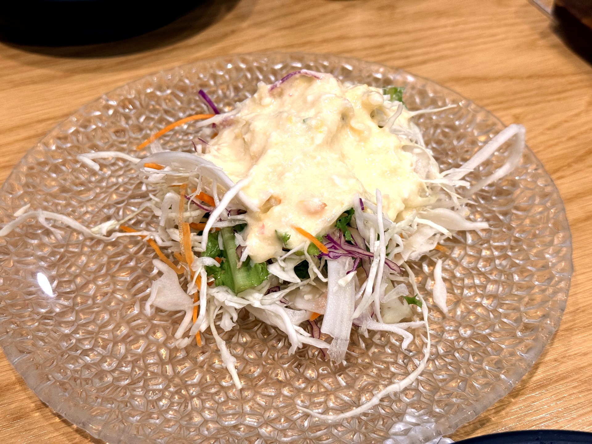 Oso Galbi salad side dish - shredded cabbage, carrot and greens topped with a creamy pale dressing on a clear textured glass plate, a starter banchan at a Korean BBQ restaurant
