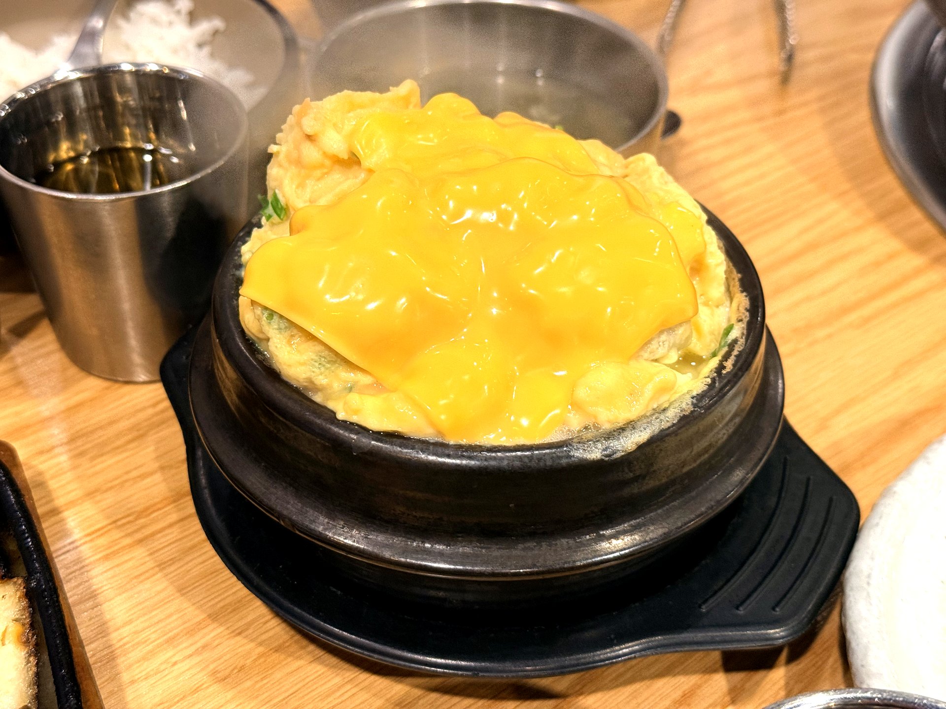 Oso Galbi 치즈 계란찜 (cheese steamed egg) - a tall, fluffy soufflé-like Korean steamed egg risen above a black stone pot, topped with a melting slice of orange cheese, at a Korean BBQ restaurant