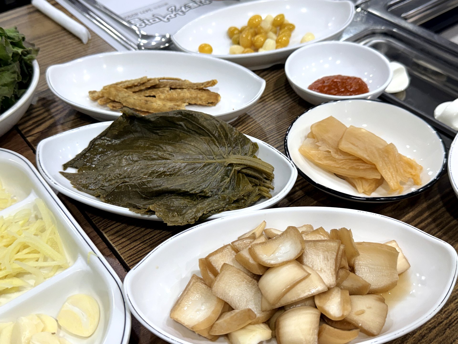 Close-up of the banchan at Hwangto Jangeo Maeul - pickled perilla leaves, crispy fried burdock, ginkgo nuts, pickled radish chunks in brine, and thin pickled radish slices on small white dishes