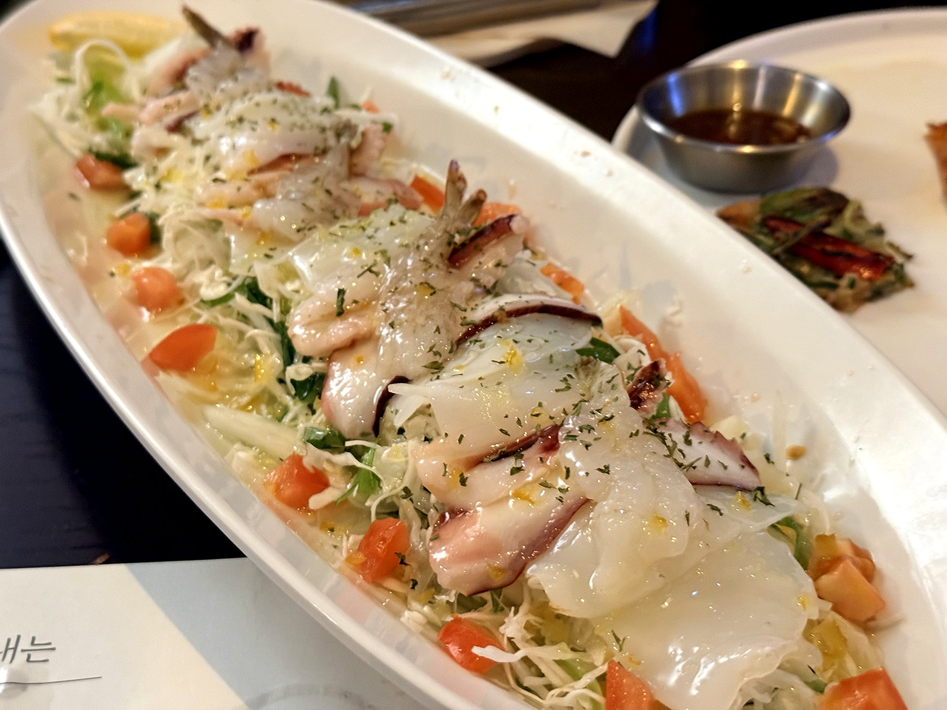 Neurin Maeul Brewery 문어숙회 샐러드 (poached octopus salad) - slices of tender white poached octopus arranged over a bed of shredded cabbage and greens with tomato pieces and a light citrus dressing, on a long white plate