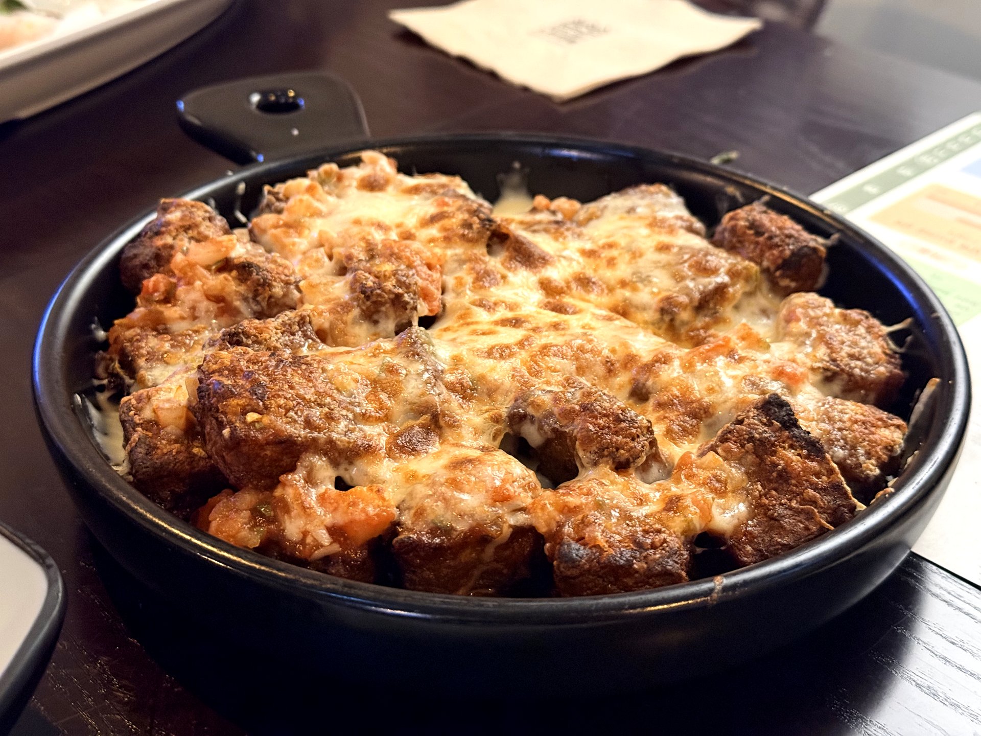 Neurin Maeul Brewery 치즈 닭함박스테이크 (cheese chicken hamburg steak) - chunks of chicken hamburg patty baked under a thick layer of golden-browned melted cheese in a round black cast-iron pan