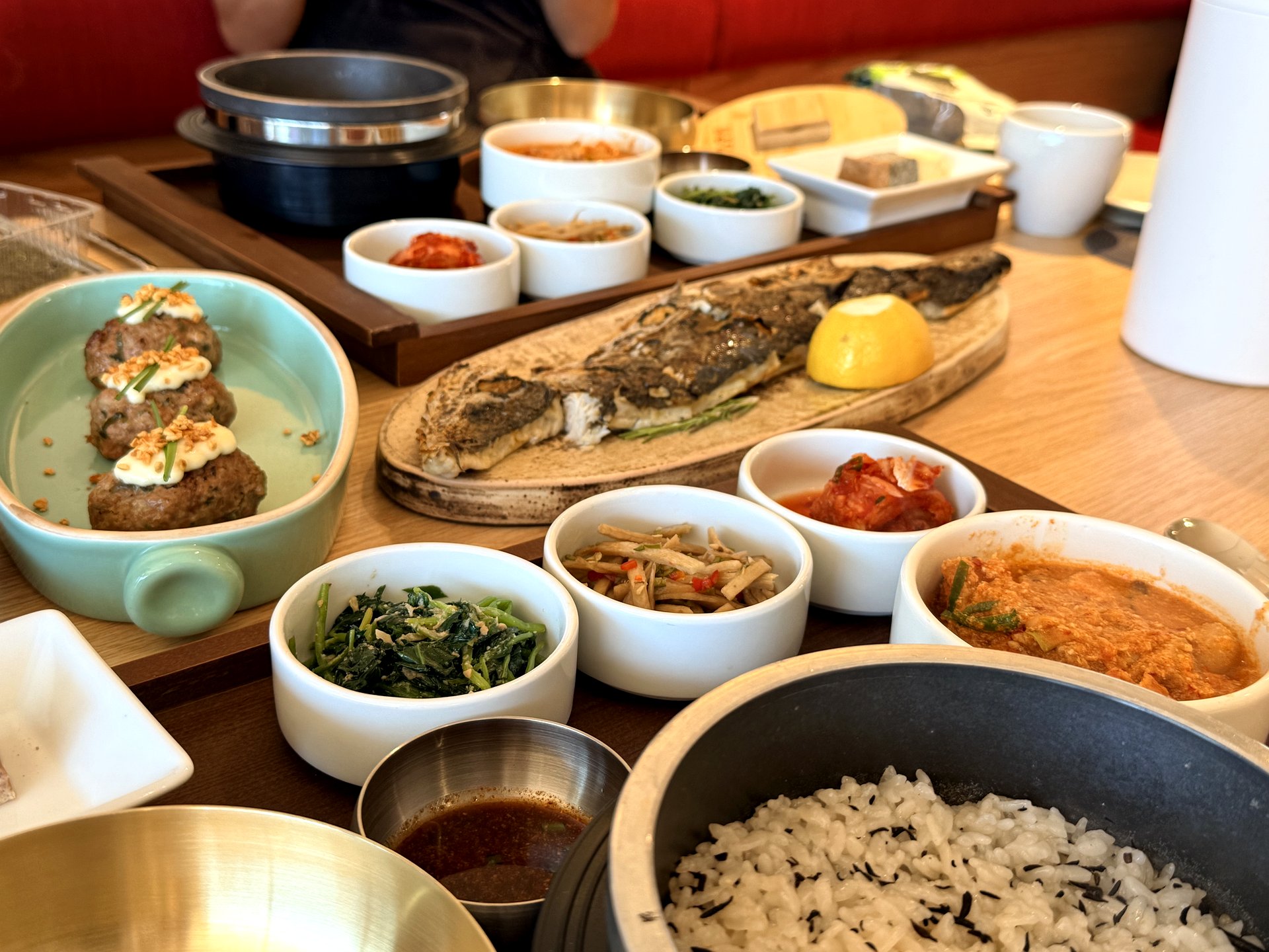 The full Ondang lunch-special spread on a wooden table - a hanwoo tteok-galbi patty, a whole grilled Spanish mackerel on an oval plate, a bubbling soybean-pulp biji stew, a bowl of hot-pot rice, and many small banchan dishes, at a Korean tofu set-meal restaurant near Seoul Station