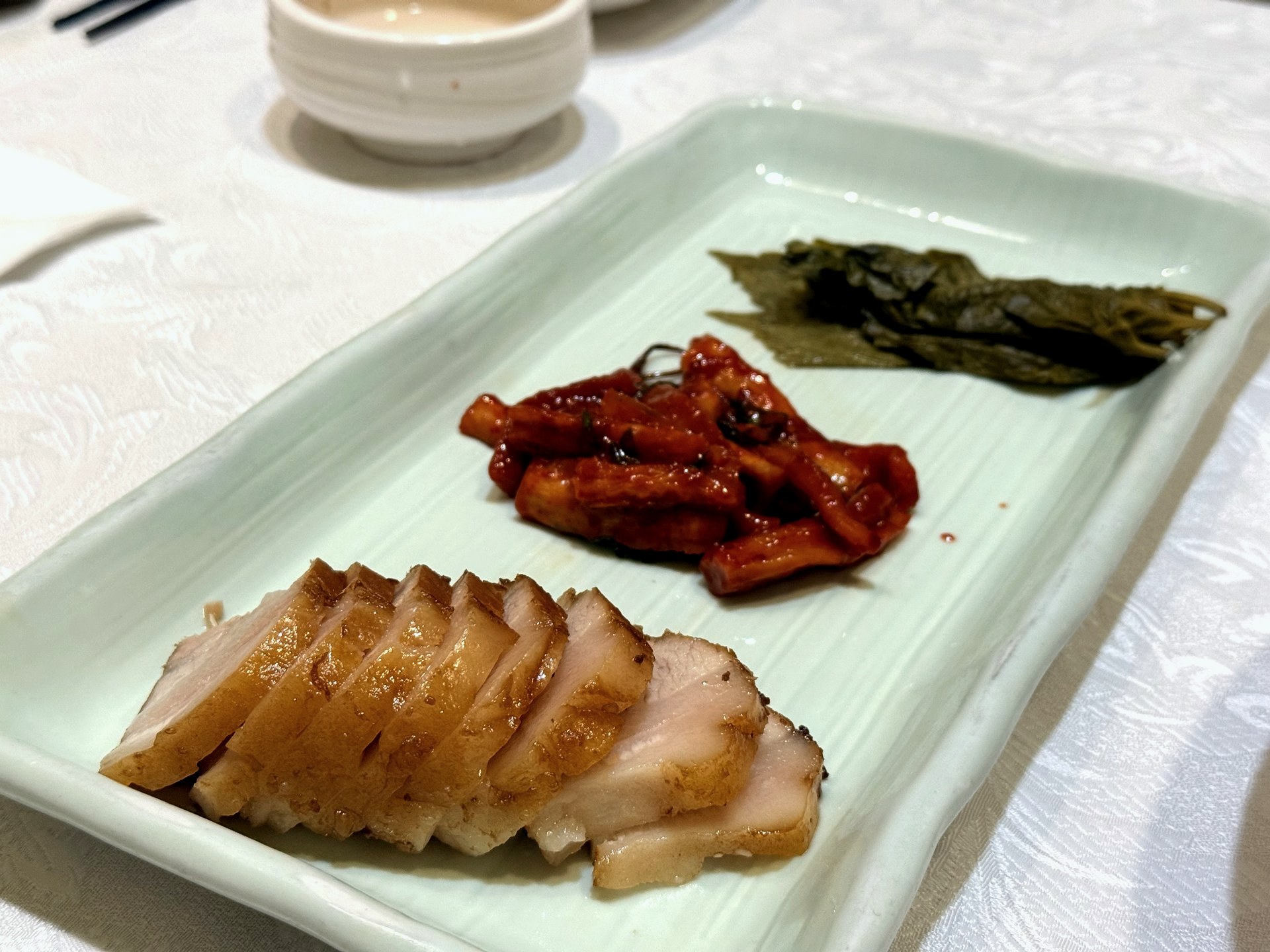 Sudam Hanjeongsik 보쌈 (bossam) - neatly sliced tender boiled pork belly on a celadon plate, served with a spicy red radish-and-seafood salad and dark pickled perilla leaves