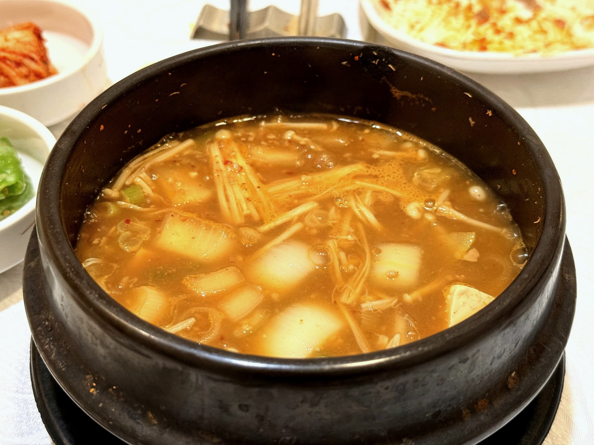 Sudam Hanjeongsik soybean-paste stew - a dark stone pot of rich reddish-brown doenjang stew with enoki mushroom, radish, tofu and scallion, bubbling hot