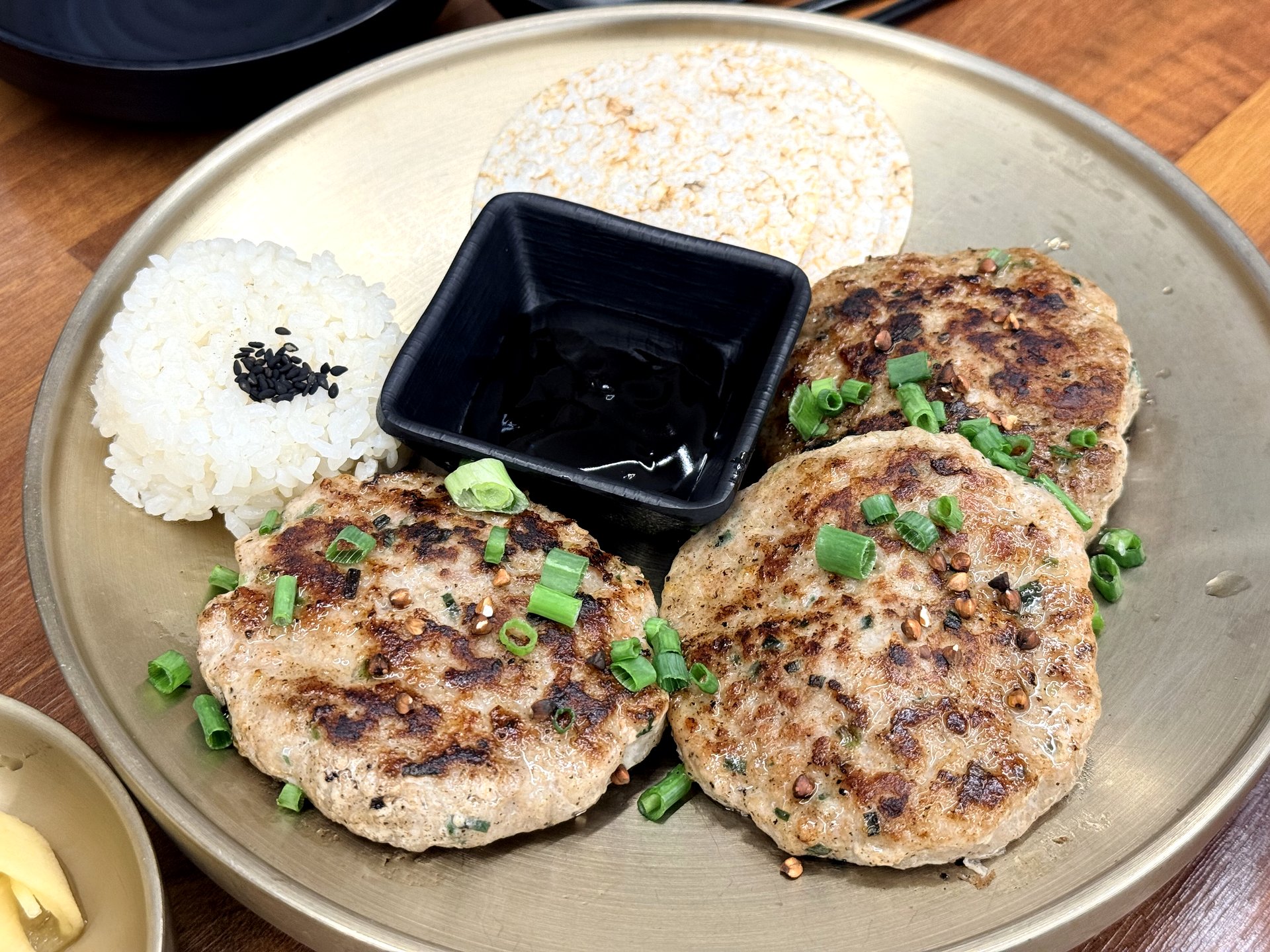 Memilbat-e Gasiri tteok-galbi - three griddled Korean minced-meat patties with scallion, served with white rice, a puffed-rice crisp and a dish of sweet soy glaze, on a brass plate