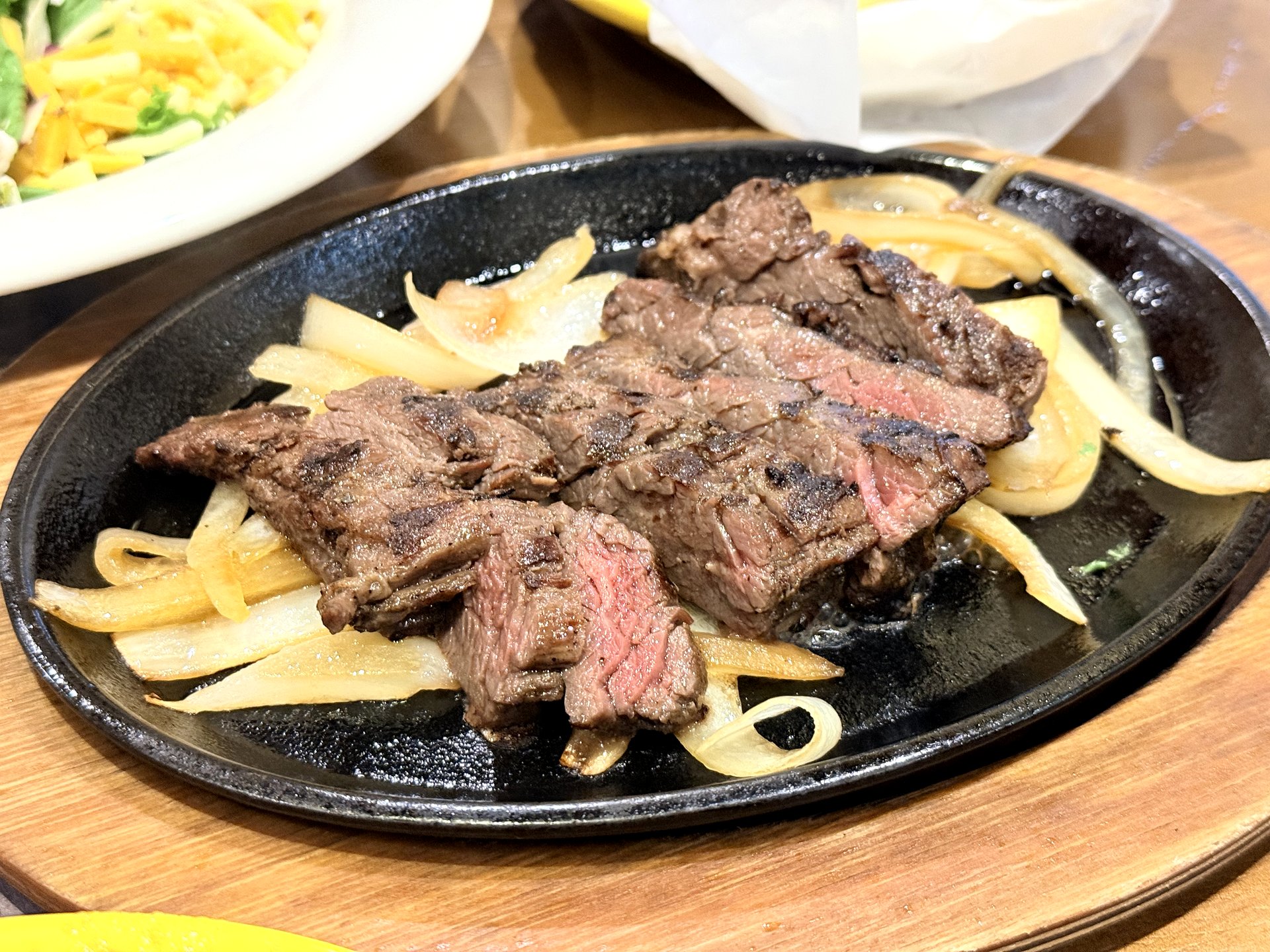 On The Border sizzling steak fajita - slices of grilled beef steak over caramelized onions on a hot black cast-iron fajita plate on a wooden board, served at a Tex-Mex restaurant